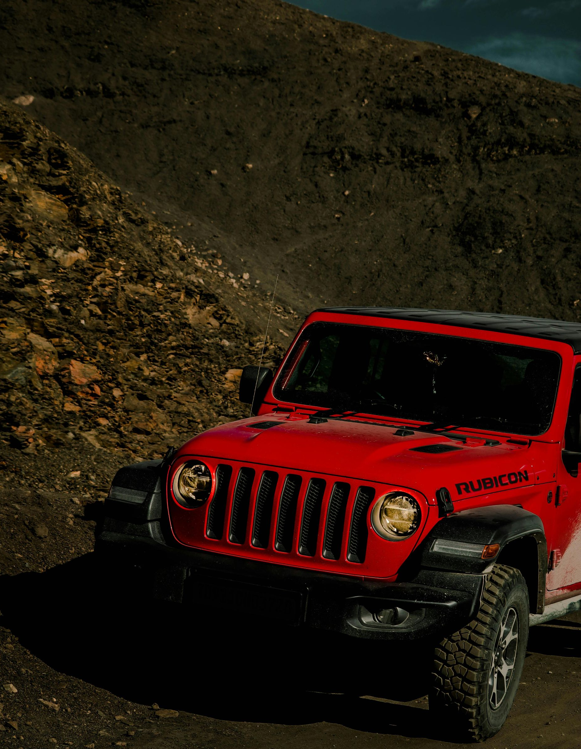 Red Jeep driving on a rocky dirt road in a rugged hillside landscape.