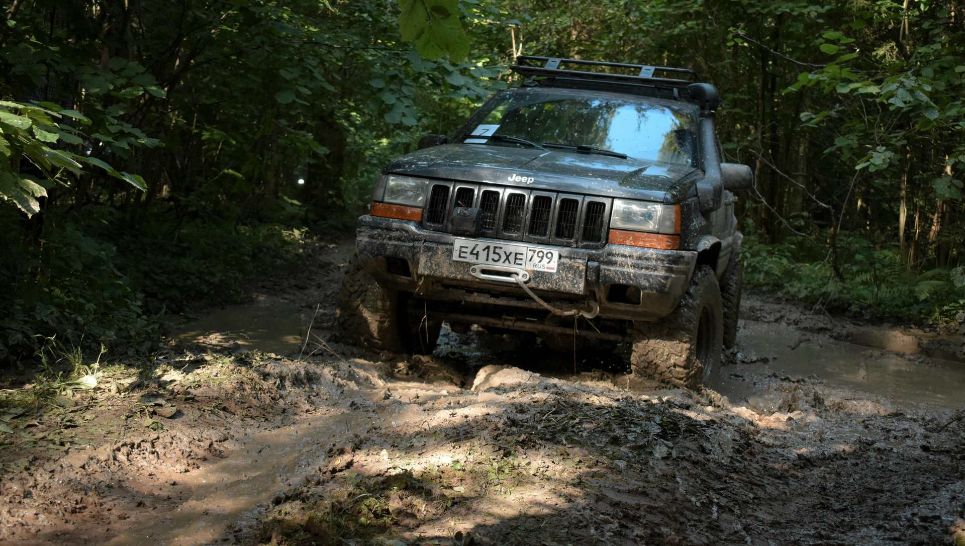 Gray SUV driving through a muddy forest trail