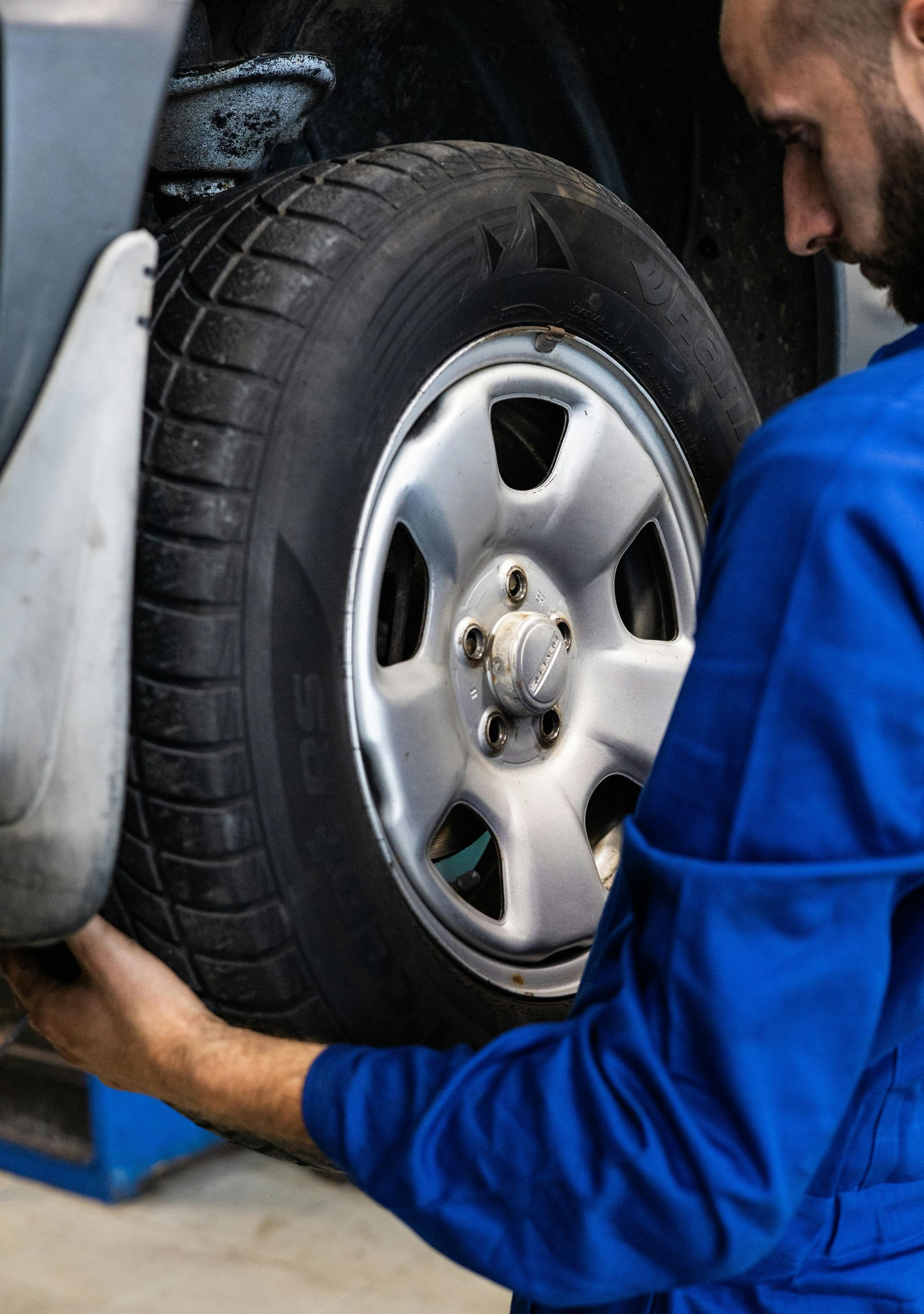 Mechanic in blue work shirt installing a car wheel tire in a garage