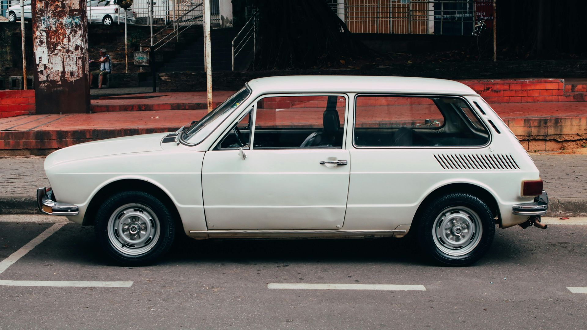 White vintage hatchback parked on a city street in front of a storefront
