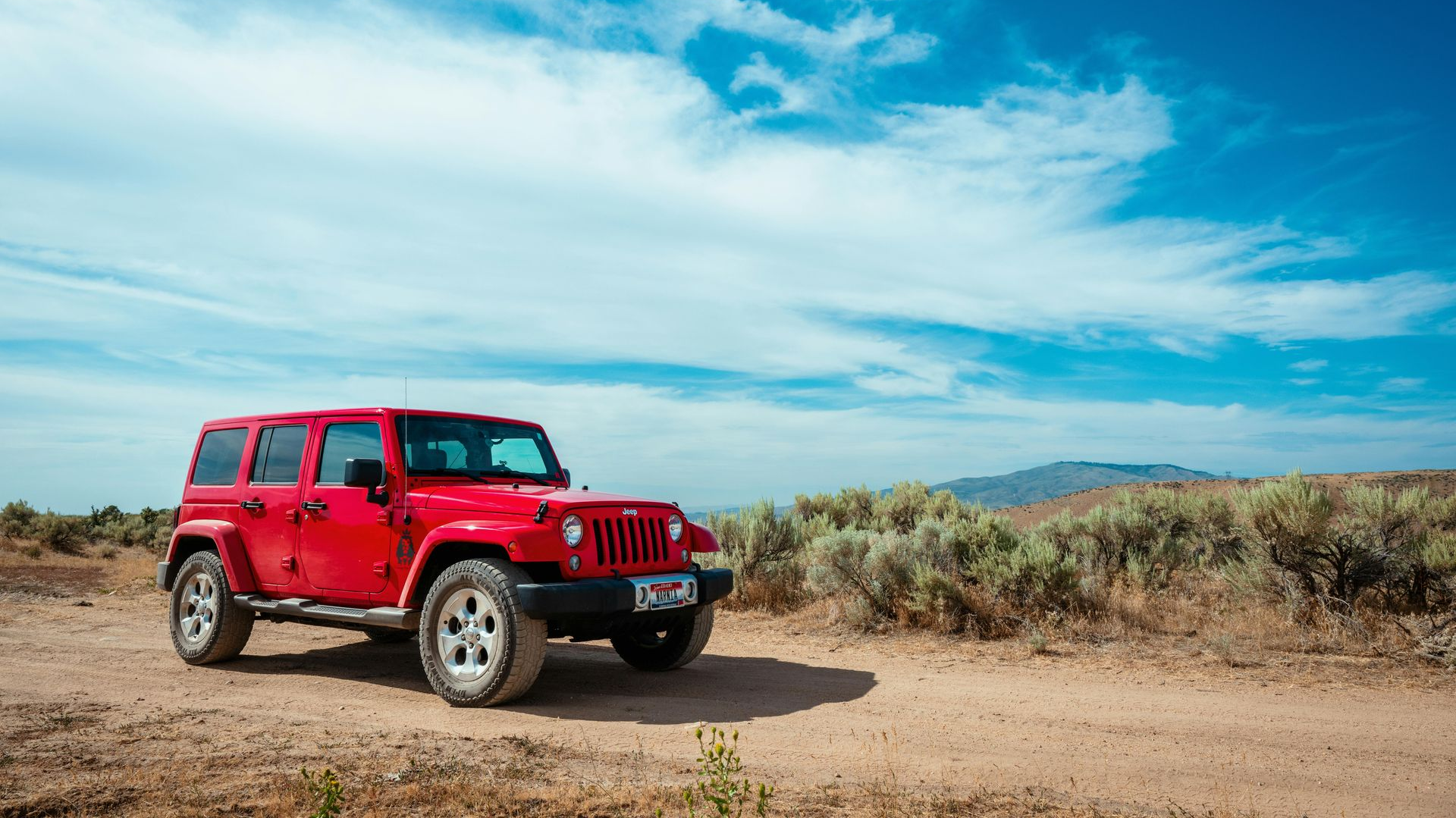 Red Jeep Wrangler on a dirt road in a desert landscape under a blue sky