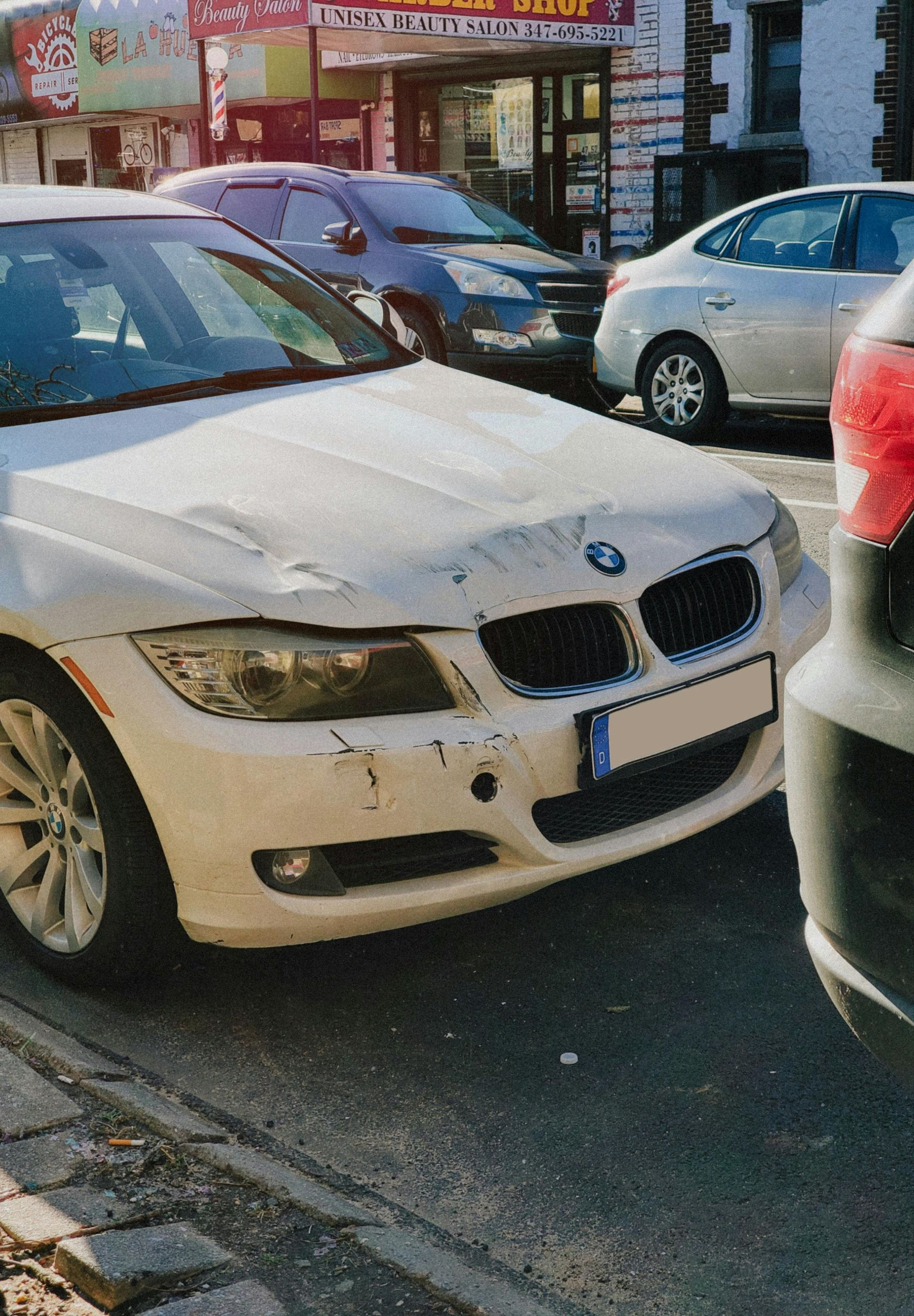 A damaged white BMW parked on a city street with other vehicles nearby.