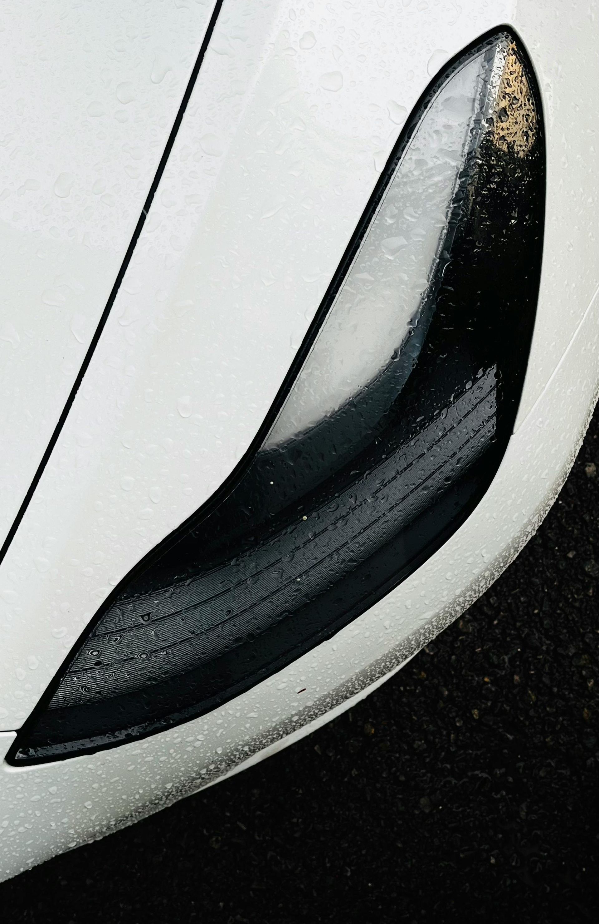 A close-up of a sleek, black car headlight set against a white, contoured vehicle body.