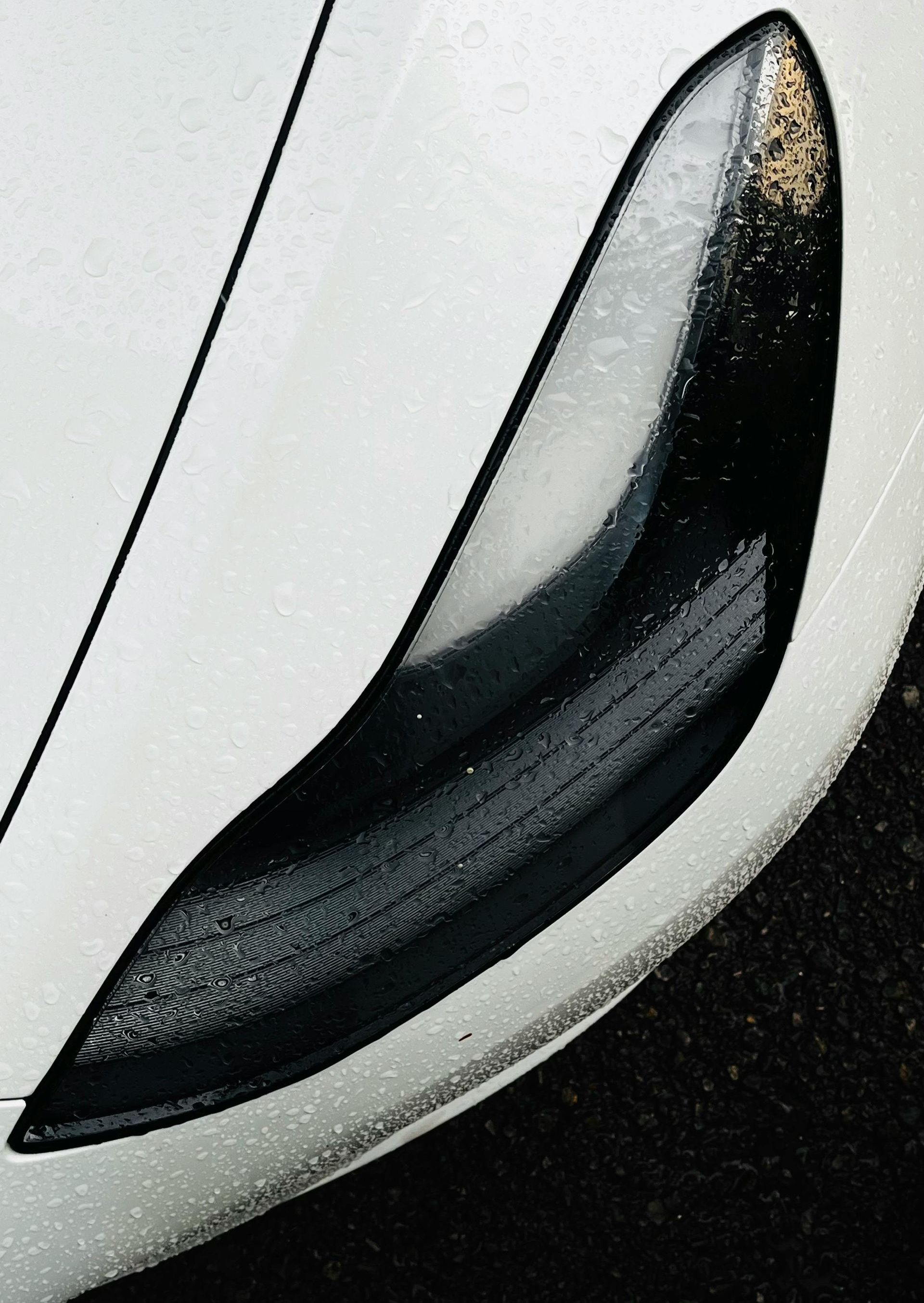A close-up of a sleek, black car headlight set against a white, contoured vehicle body.