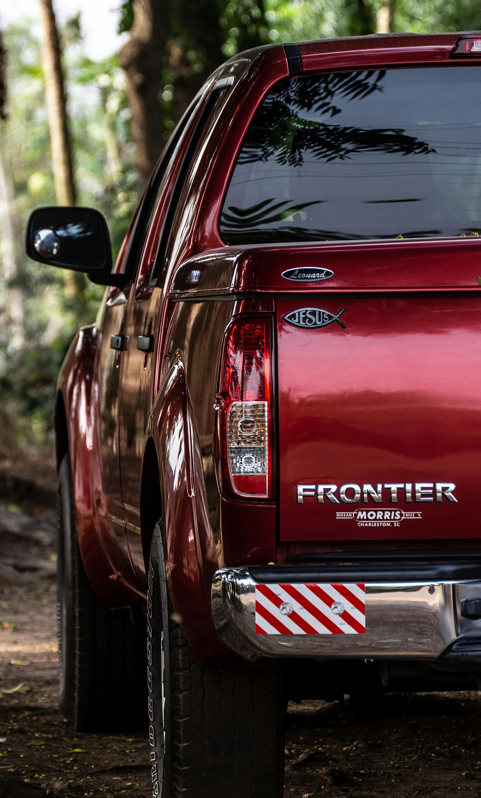 Rear view of a red Isuzu Frontier pickup truck parked outdoors on a dirt path