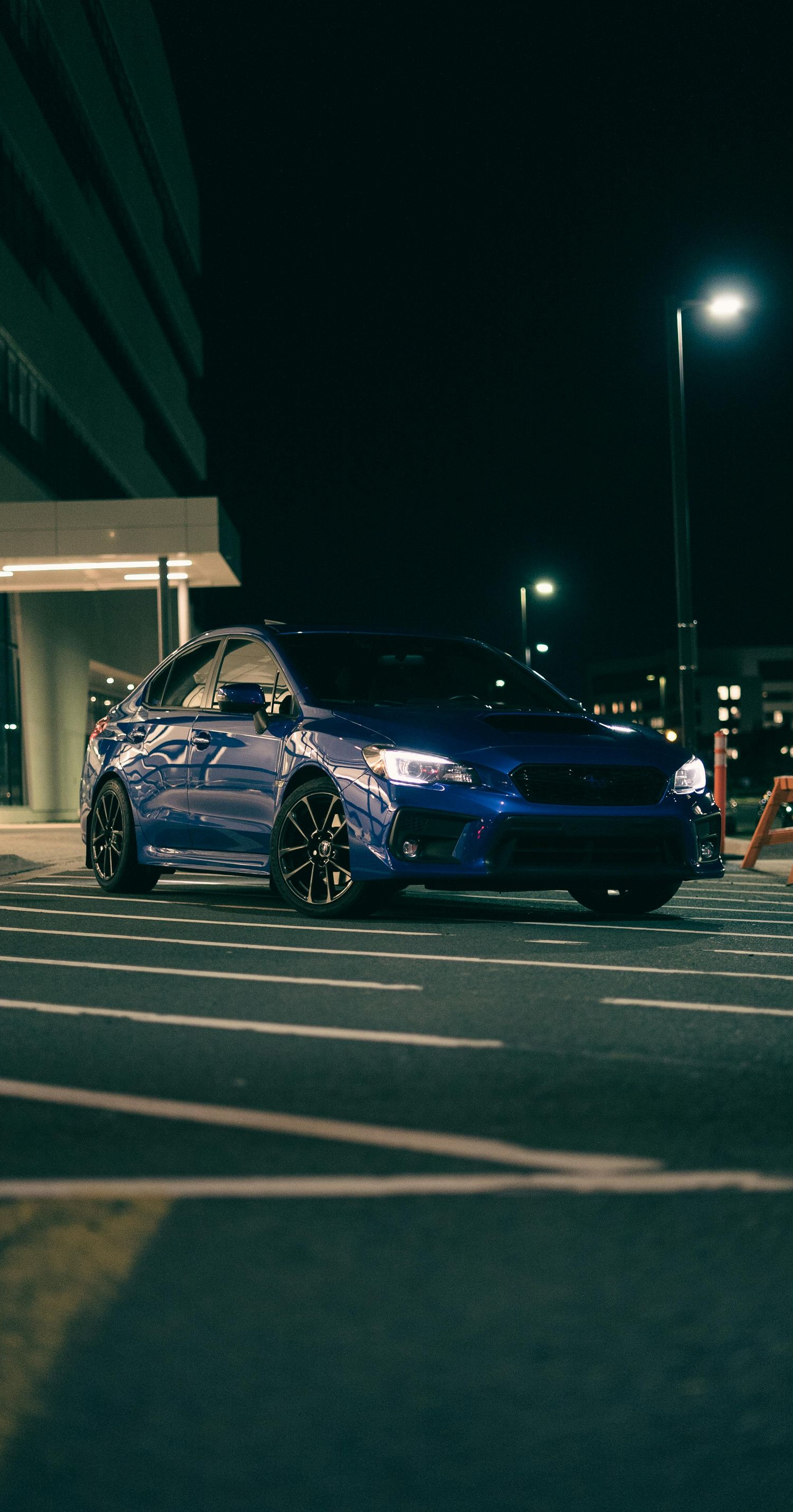 Blue car parked at night on a city street beside a building and streetlights