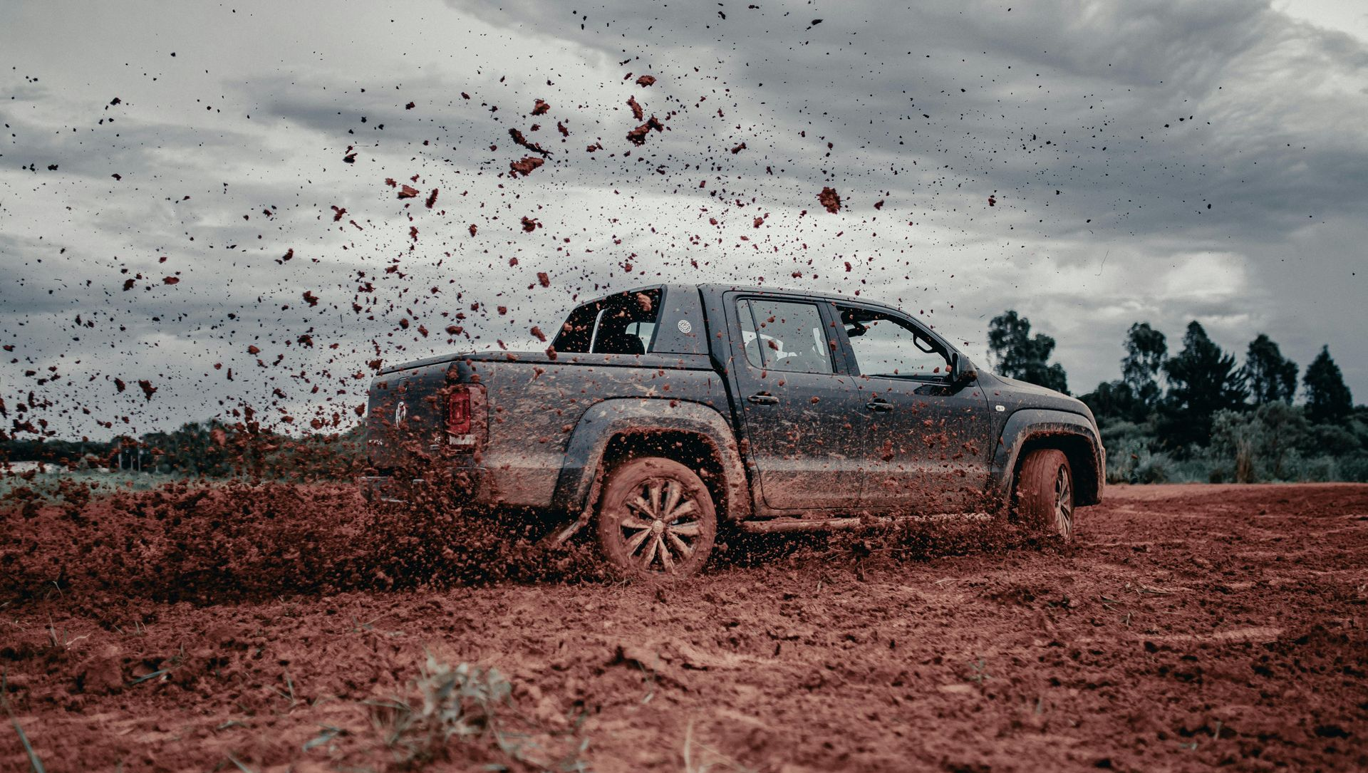 Gray pickup truck splashing through muddy terrain under a cloudy sky