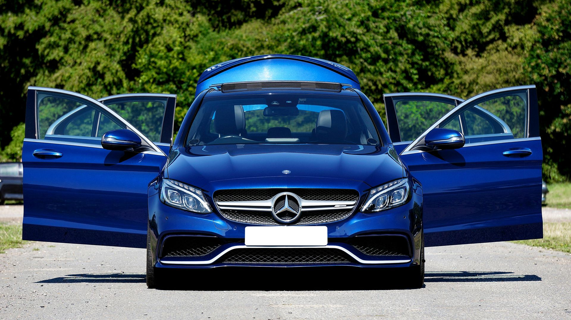 Blue Mercedes sedan with both front doors open, parked outdoors in daylight