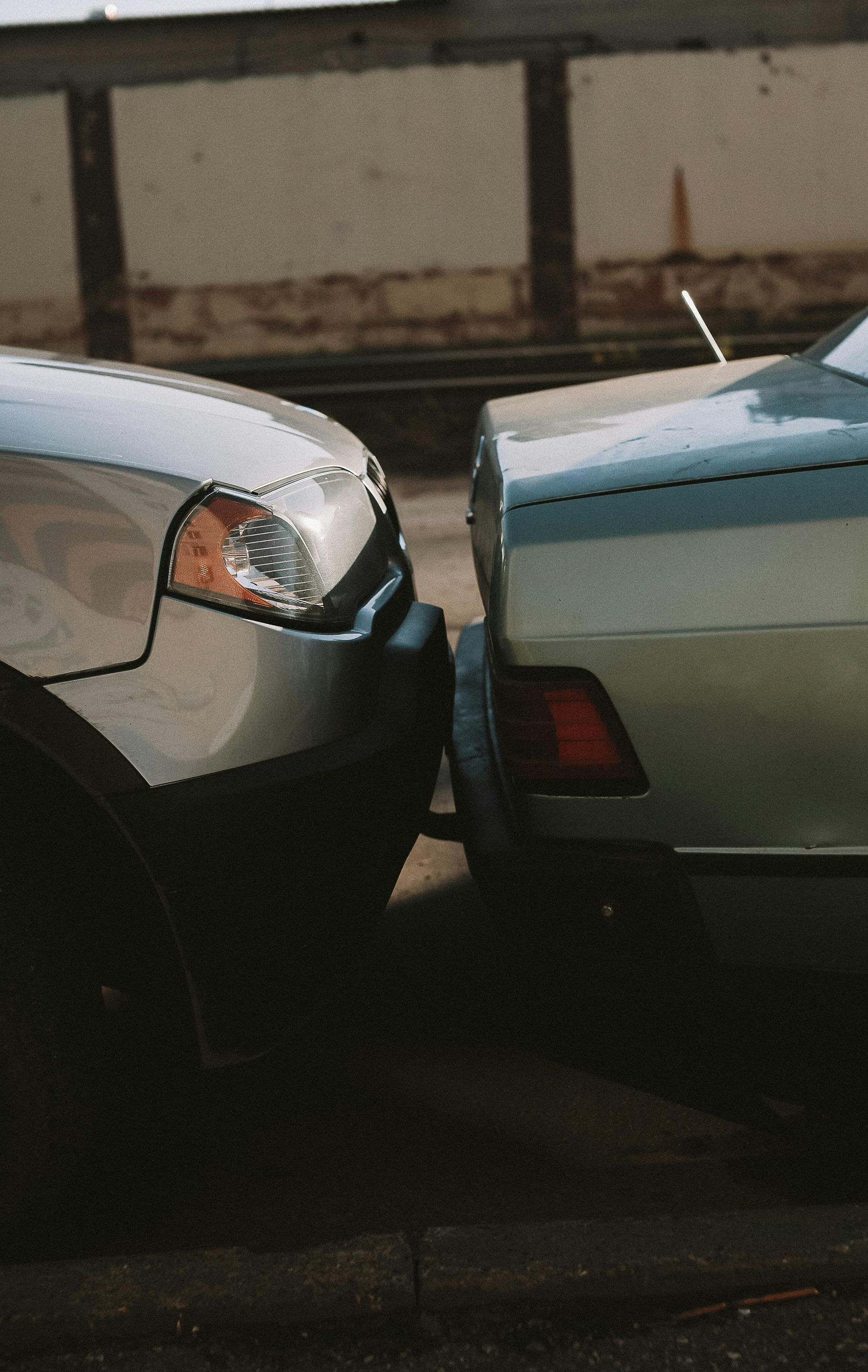 A light-colored SUV is bumped against the rear bumper of a metallic green sedan on an asphalt street.
