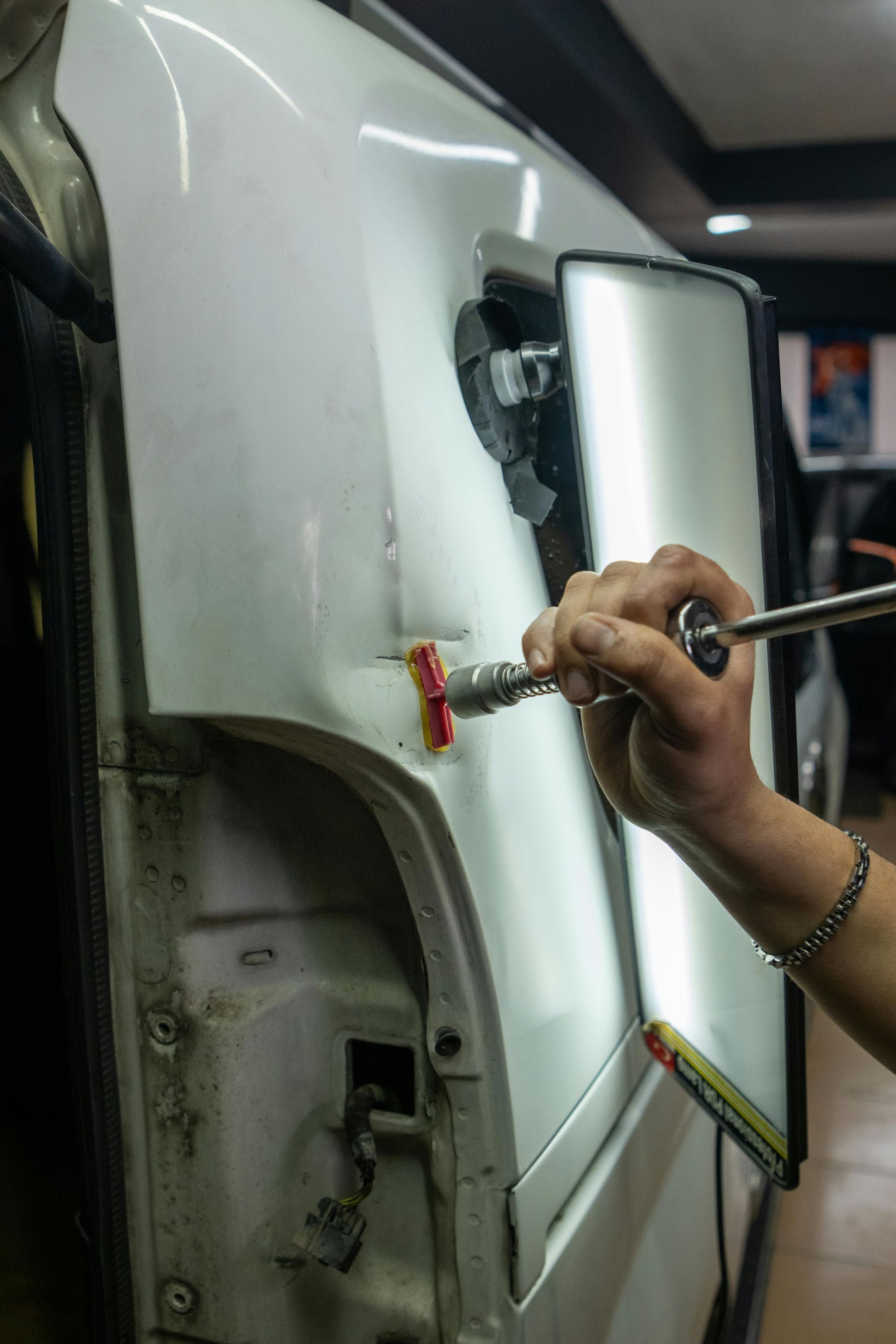 Person using a tool to repair a dent in a white car panel.