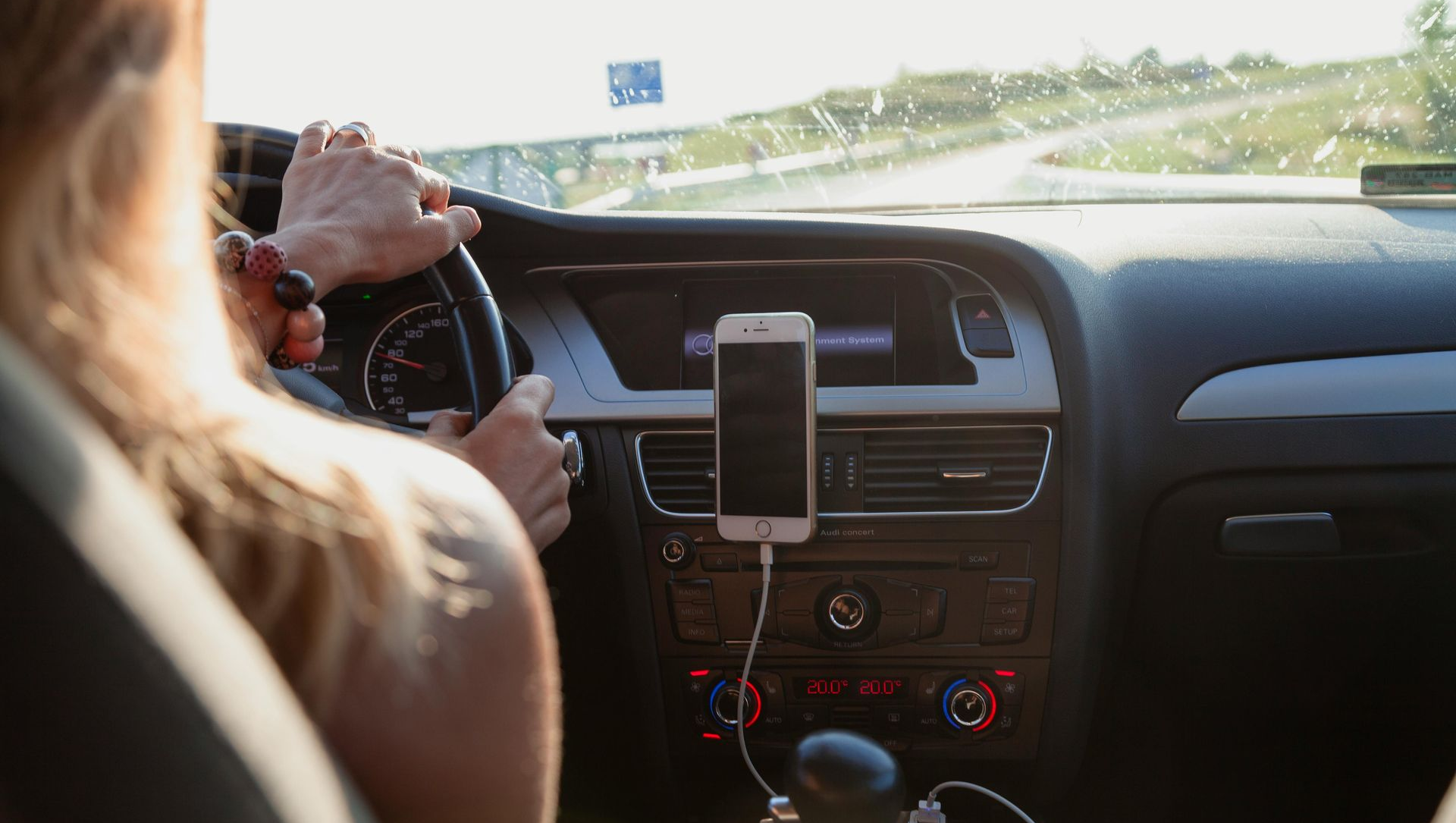 Person driving a car, hands on steering wheel. Phone mounted on the dashboard. Road visible through windshield.