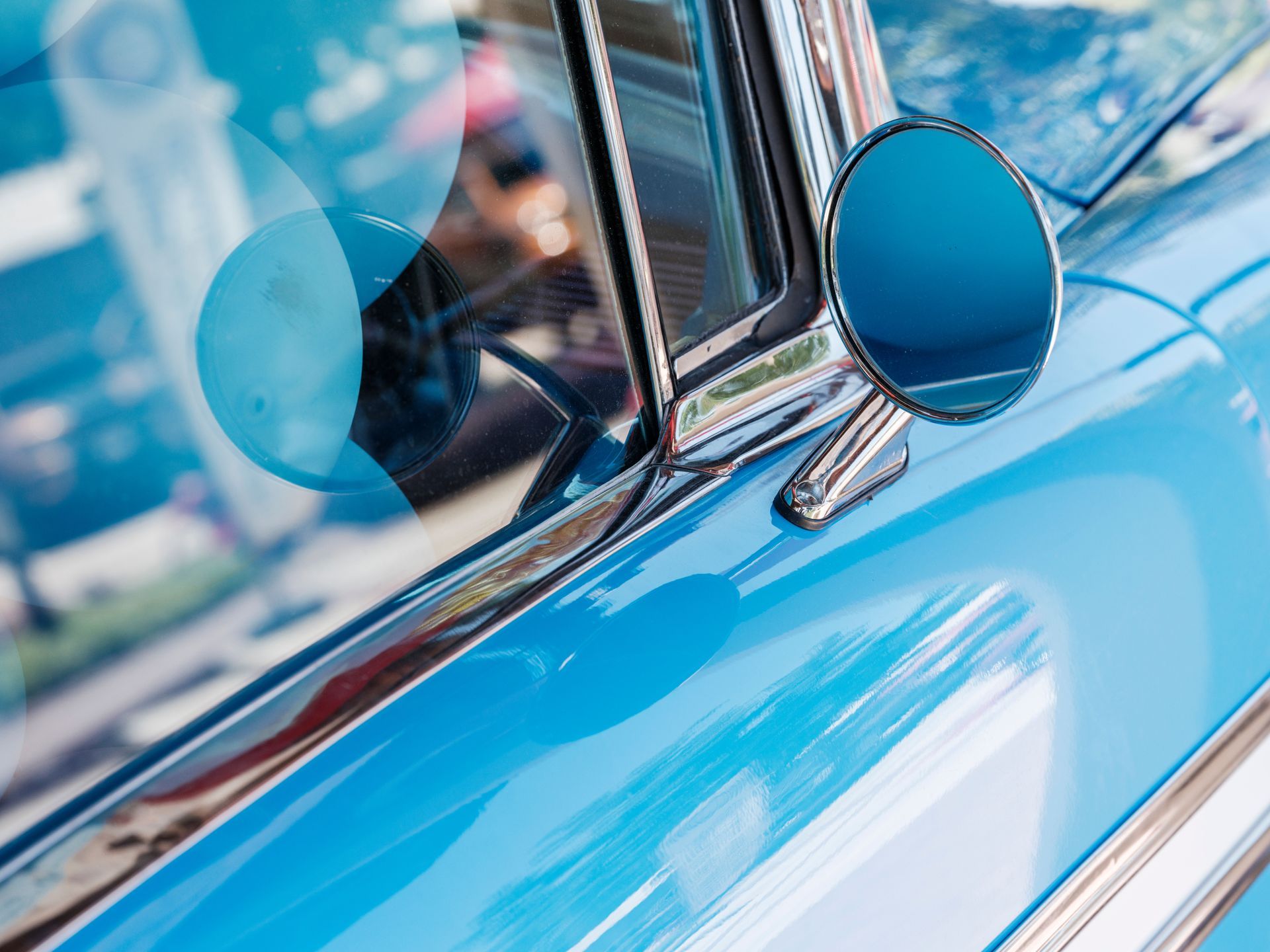 Close-up of a shiny blue vintage car door and chrome side mirror.