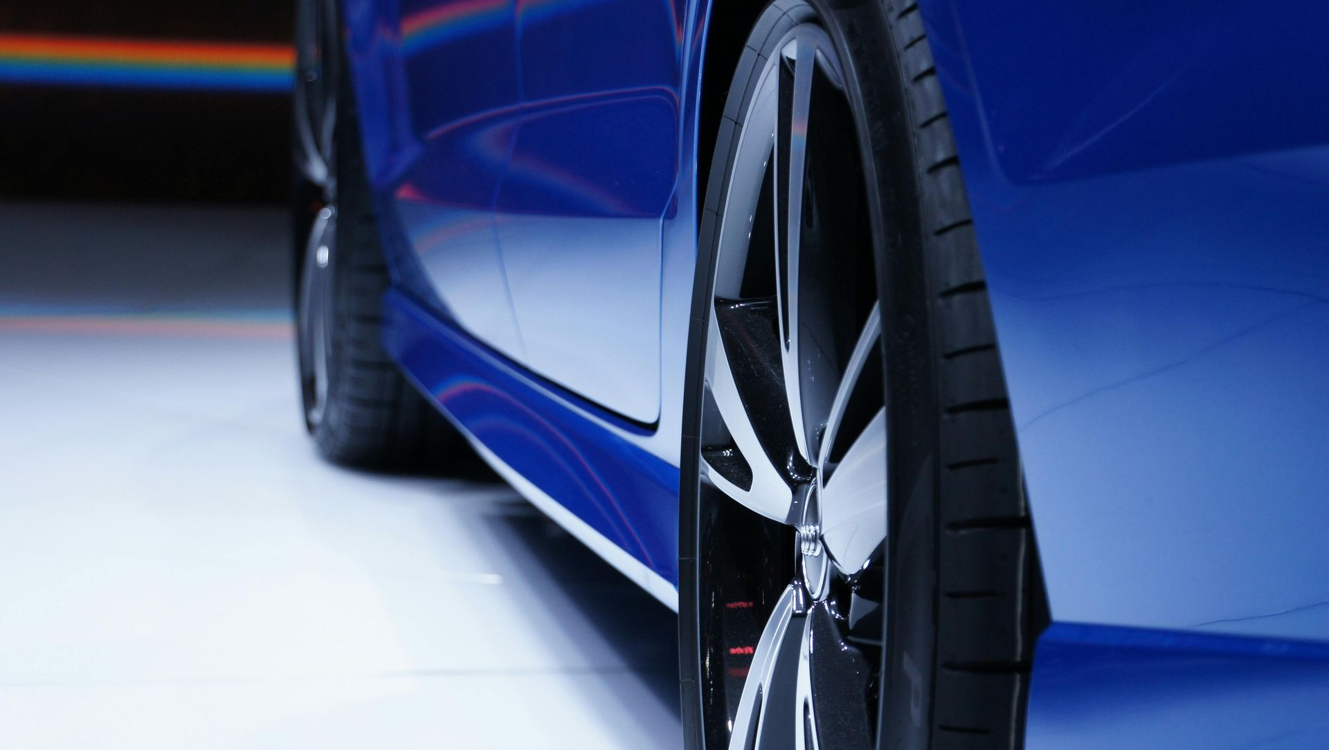 Close-up of a blue car, focusing on the alloy wheels and low-profile tires against a bright, minimalist background.