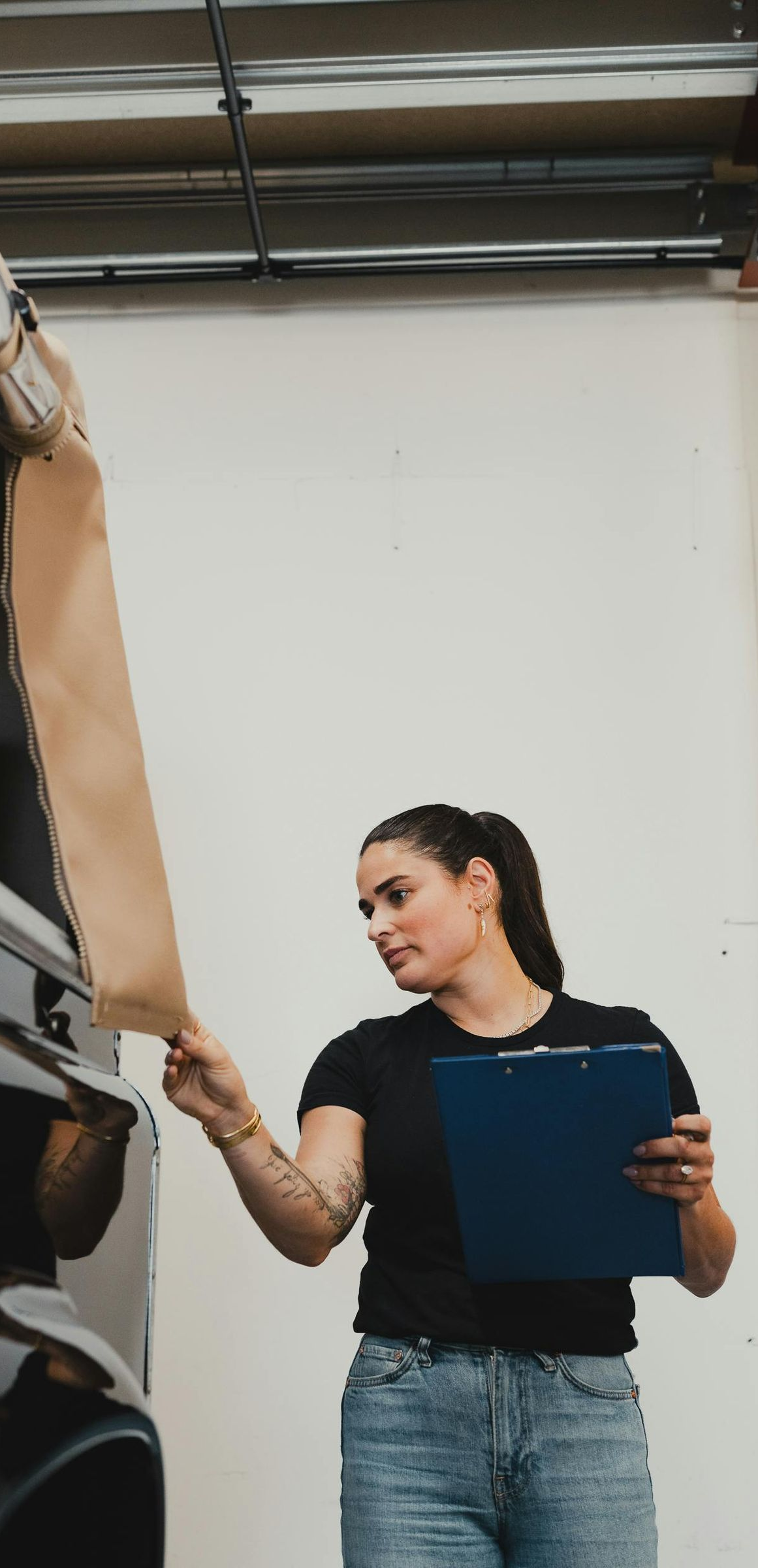 Person in a gym holding a blue clipboard beside weight equipment, reaching toward a tan strap.