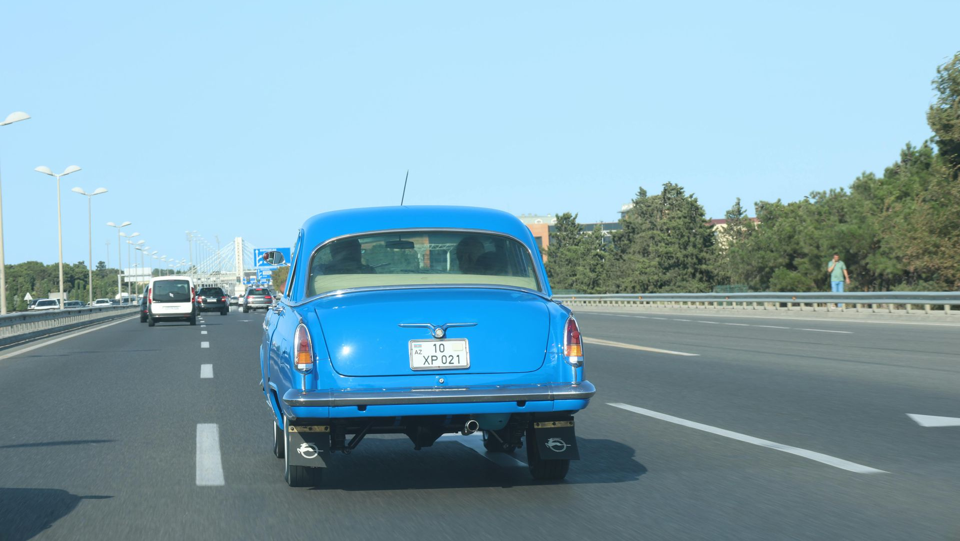 Bright blue vintage car driving on a highway under a clear sky