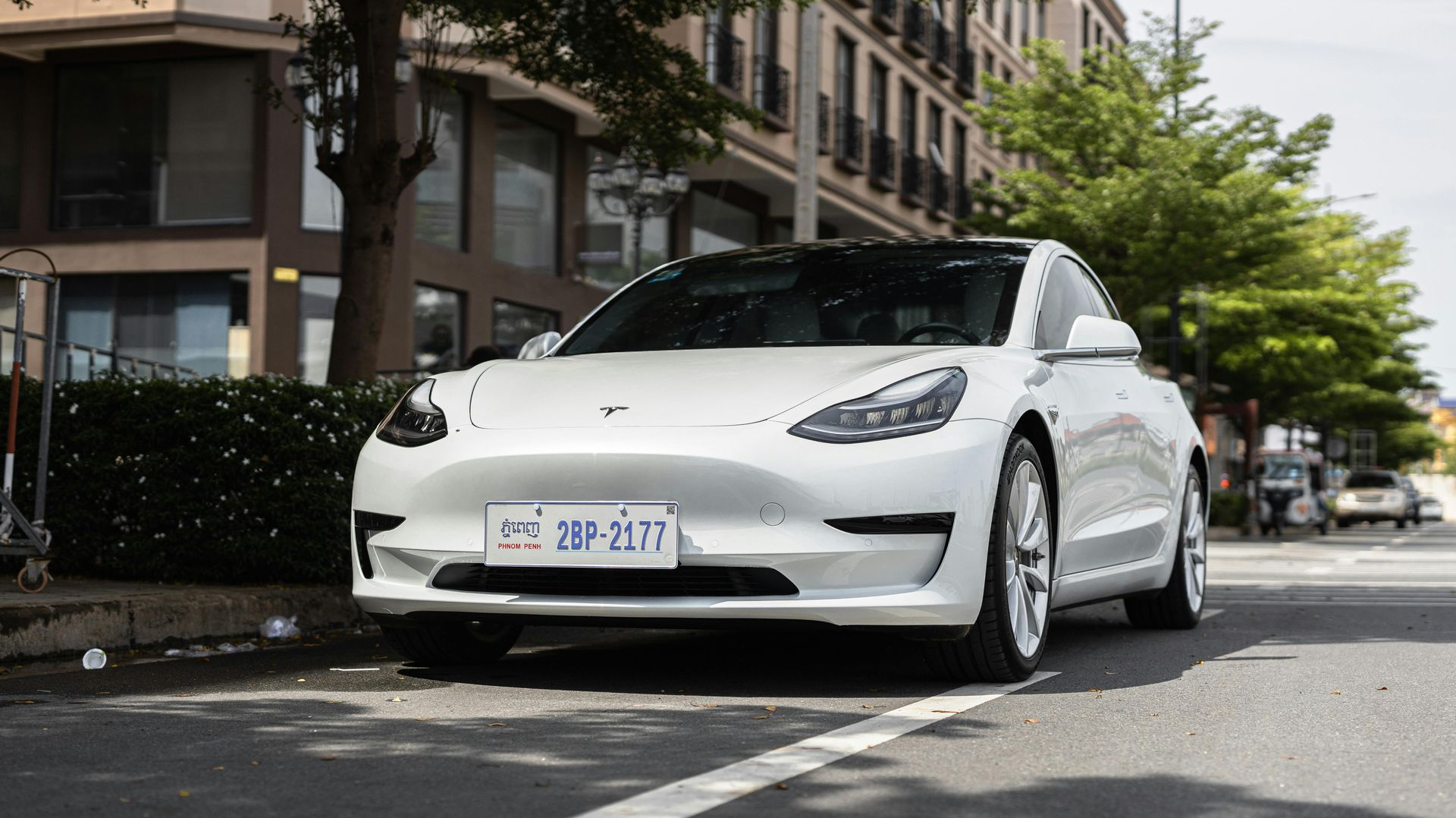 White Tesla sedan parked on a city street beside apartment buildings and trees.
