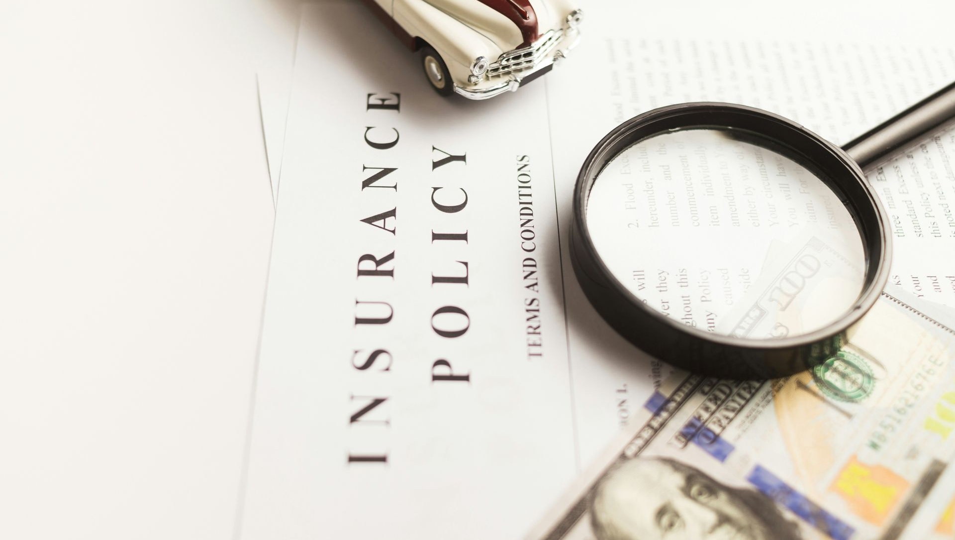 A toy car, a magnifying glass, and a $100 bill rest on a document titled