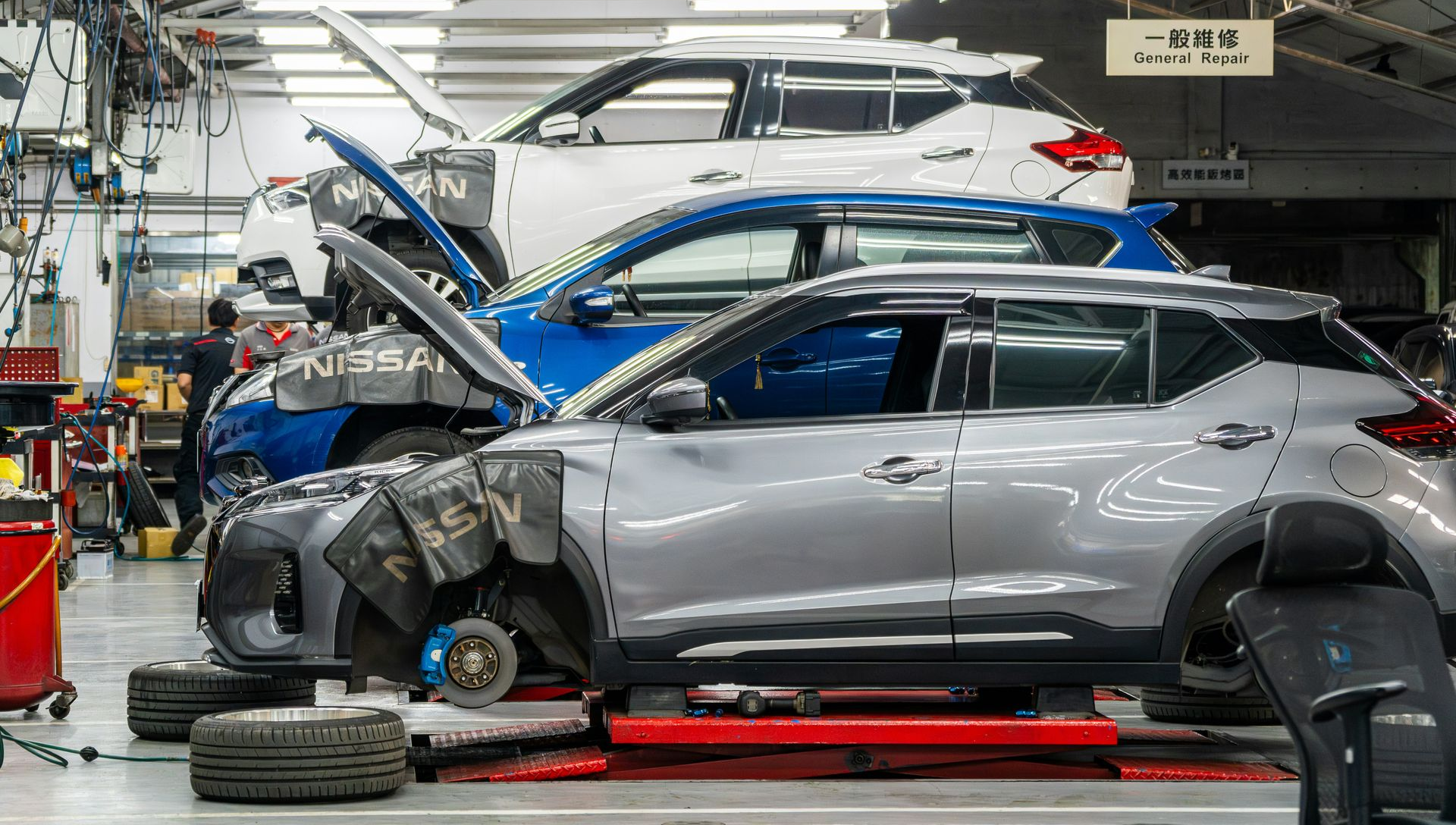 Silver SUV with front-end damage in an auto repair shop, raised on a lift with tools and parts nearby