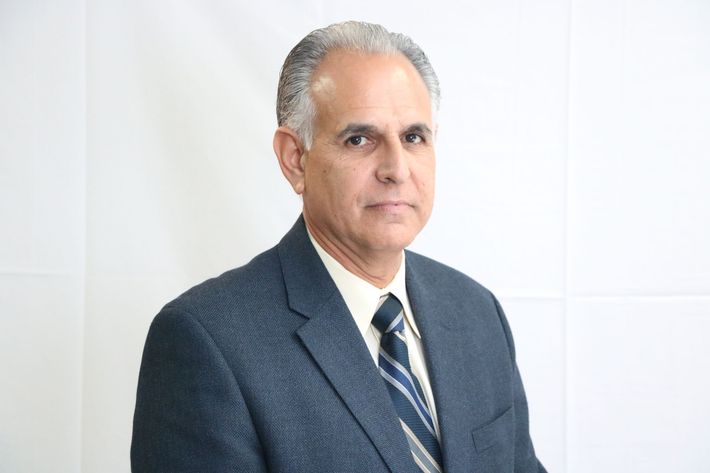 Man in a blue suit, light shirt, and tie against a white background; looking at the camera.