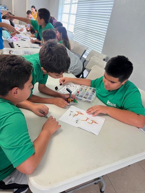 Children in green shirts building with colorful blocks at a table.