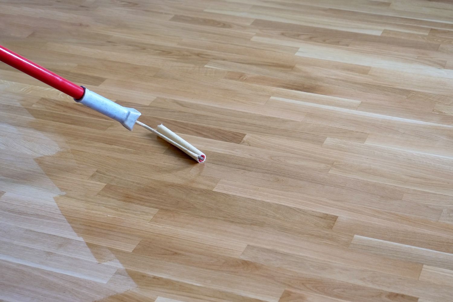 A person is painting a wooden floor with a roller.