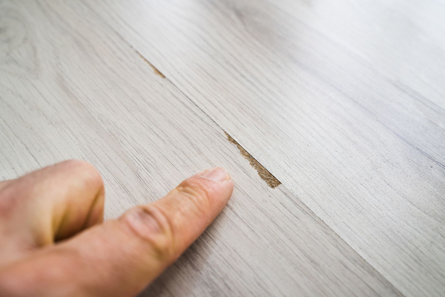 A person is pointing at a hole in a wooden floor.