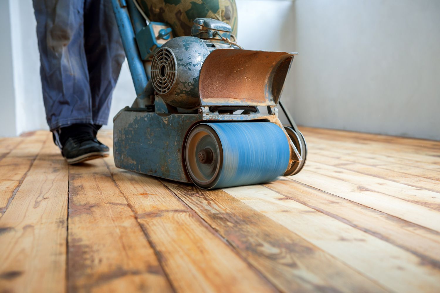 A man is sanding a wooden floor with a machine.