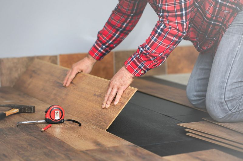 A man in a plaid shirt is installing a wooden floor. A man in a plaid shirt is installing a wooden floor.