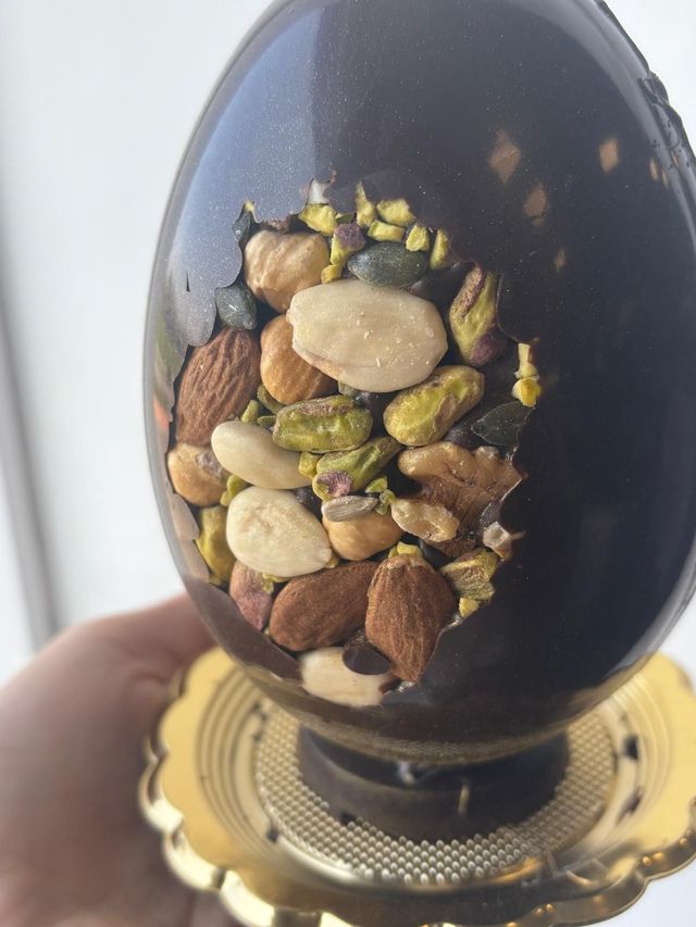 Uovo di Pasqua di cioccolato ripieno di noci, tenuto su un supporto dorato.