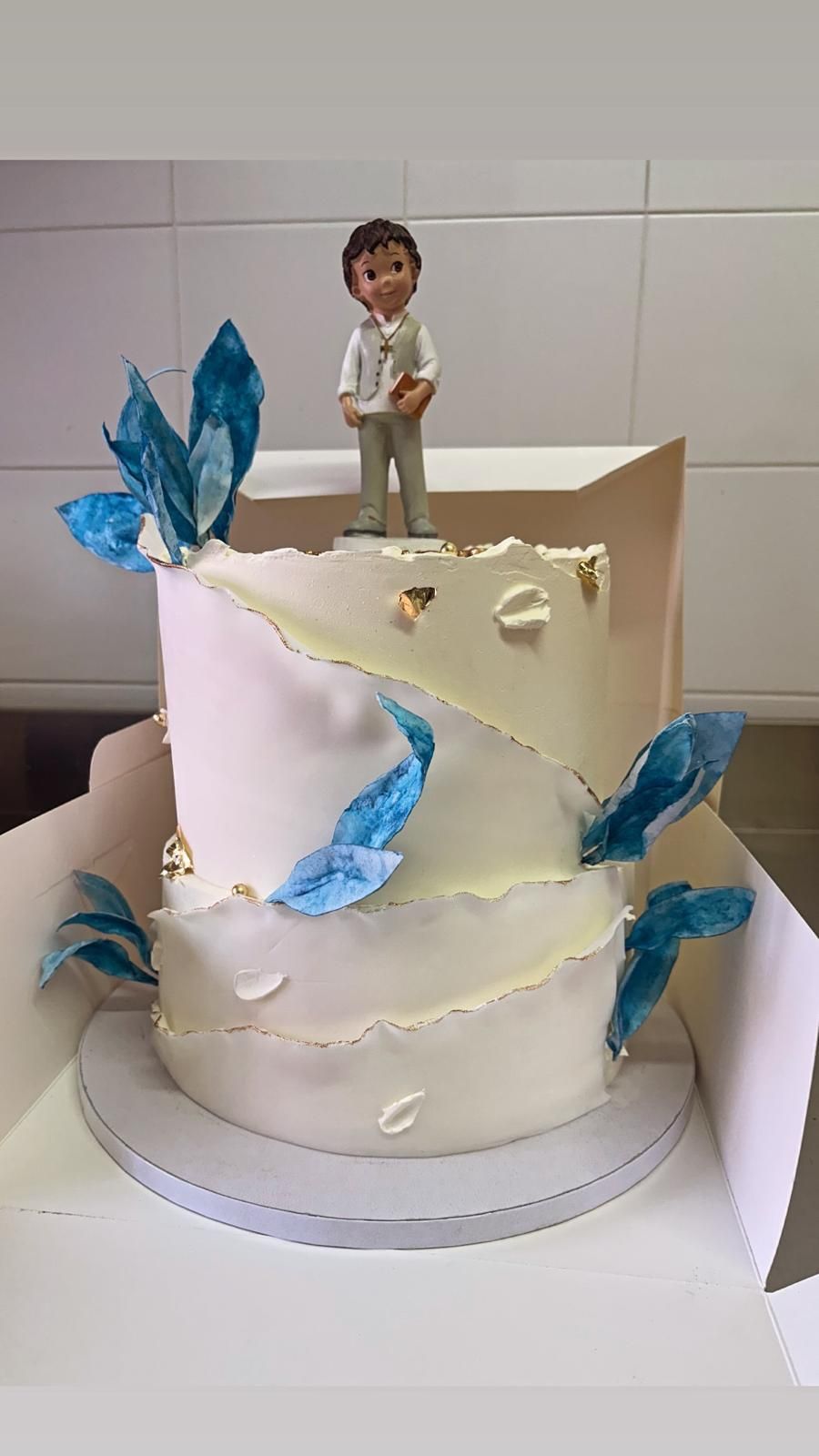 Torta bianca a due piani decorata con dettagli blu e con una statuina in cima.