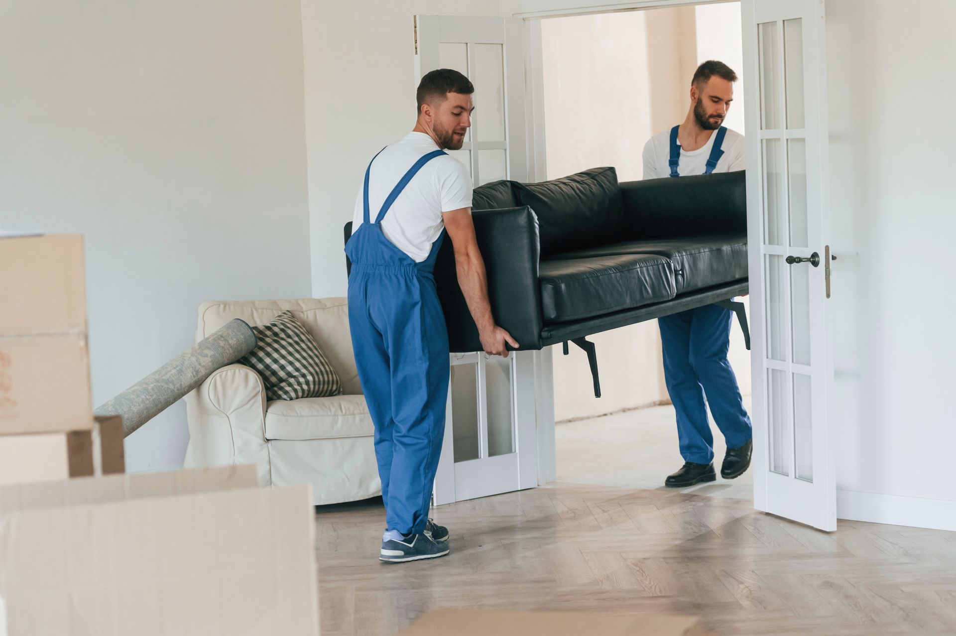 Two men are carrying a couch in a living room.