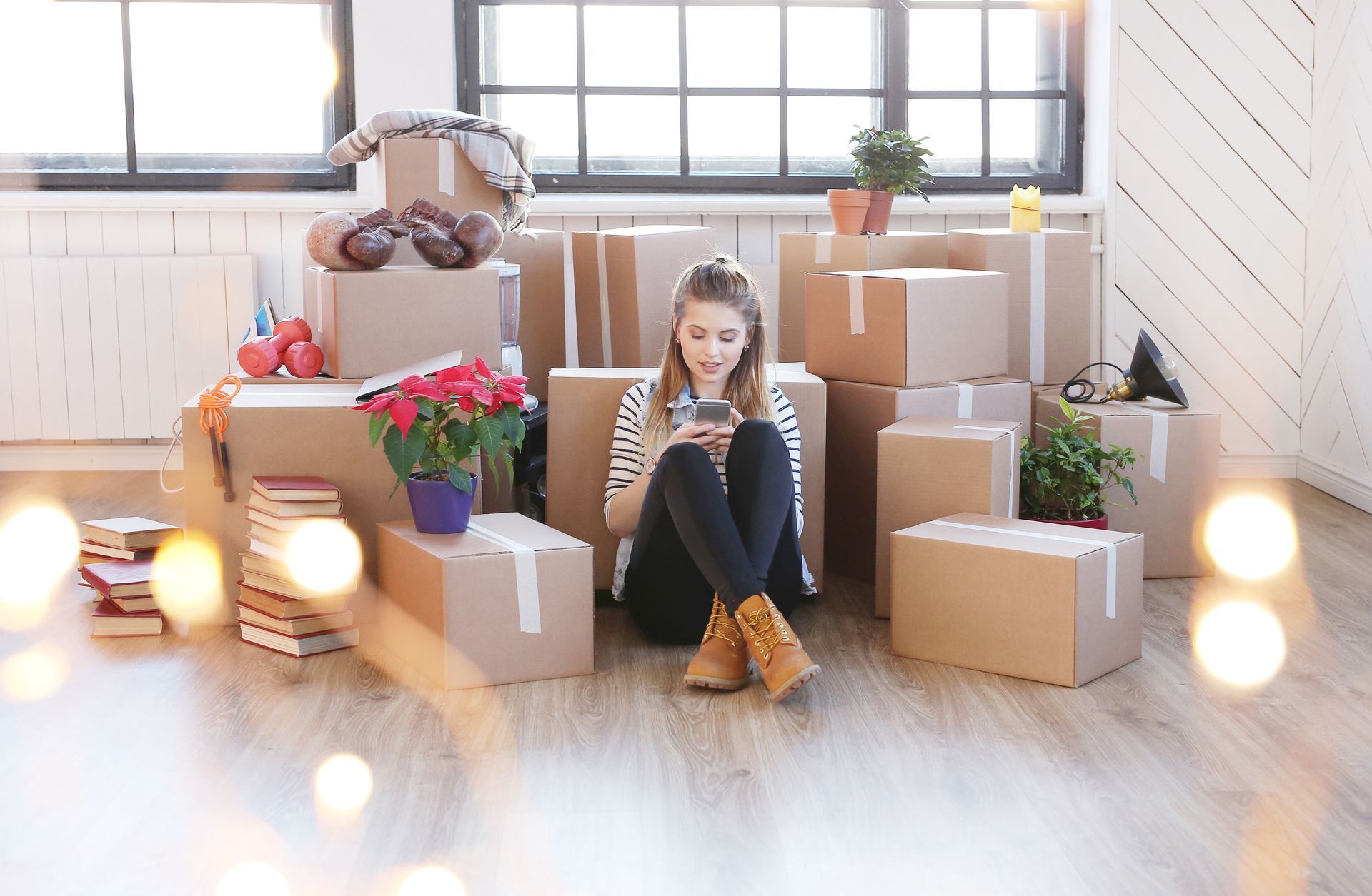 A woman is sitting on the floor surrounded by cardboard boxes and using a cell phone.