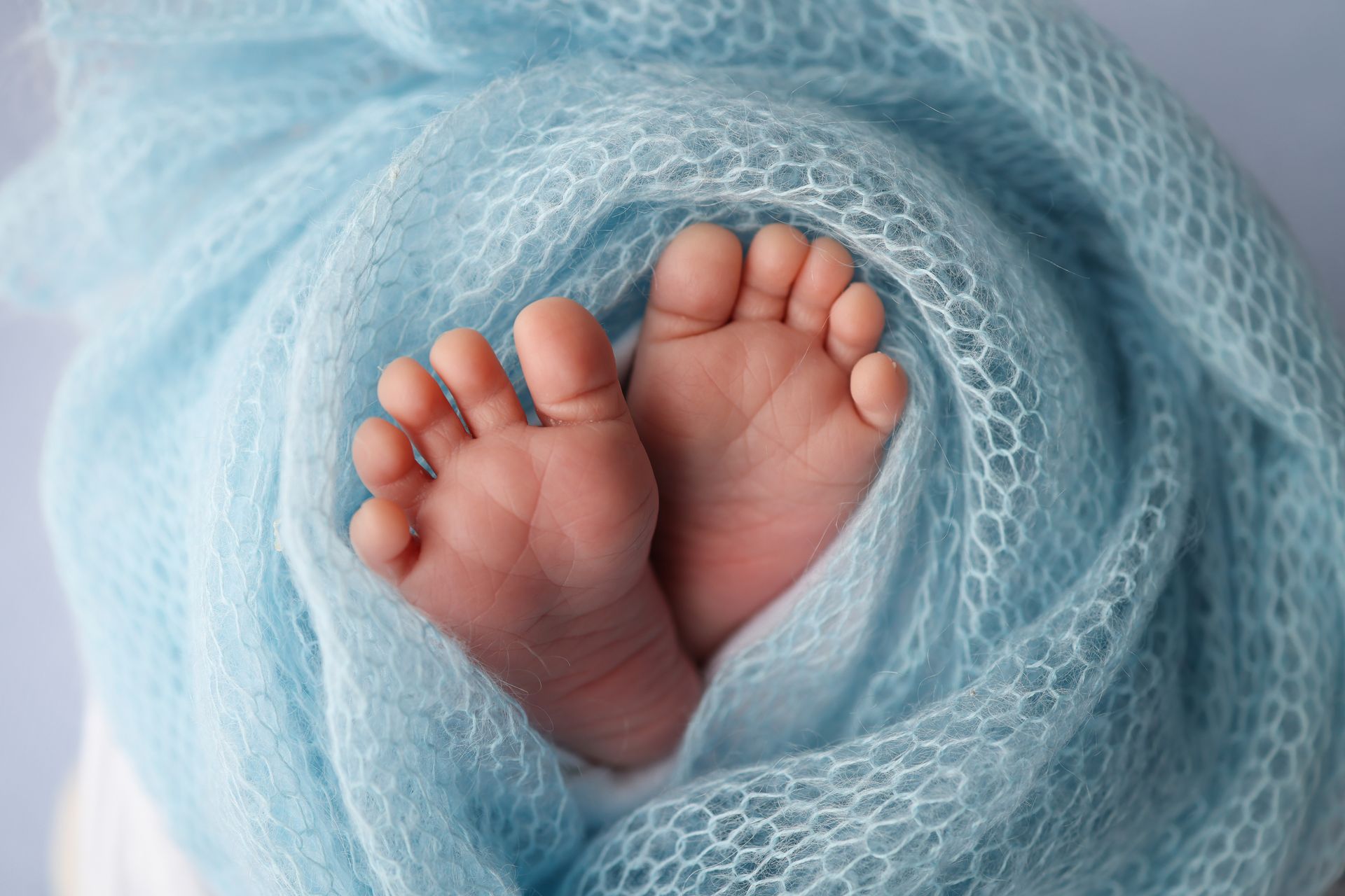 Baby's feet sticking out and wrapped up in a blue blanket.