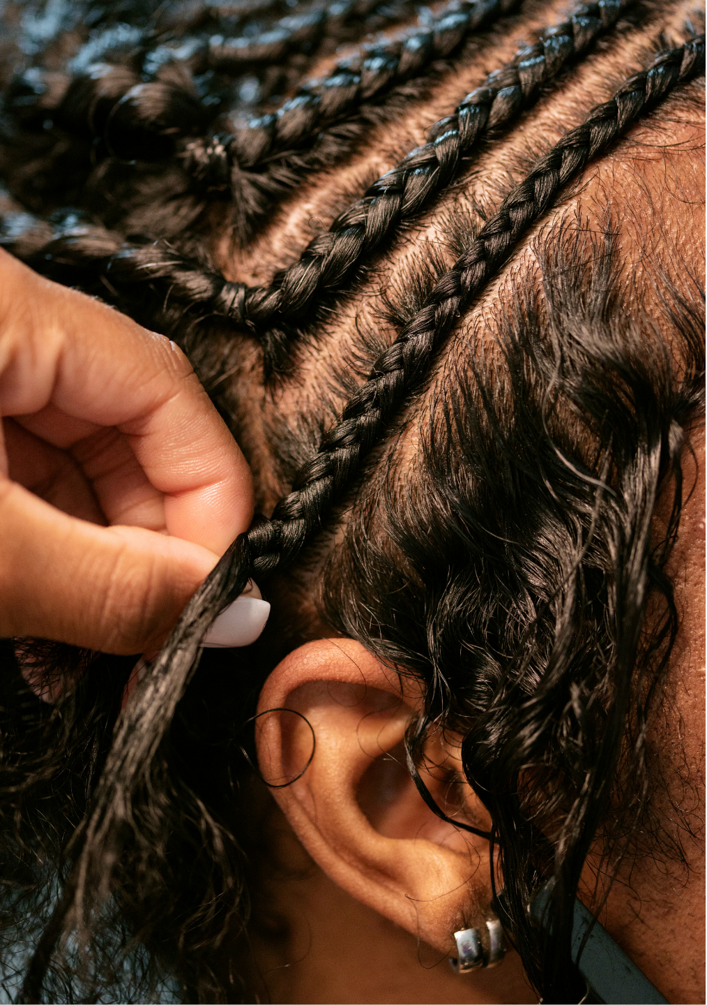 A close up of a person braiding a woman 's hair.