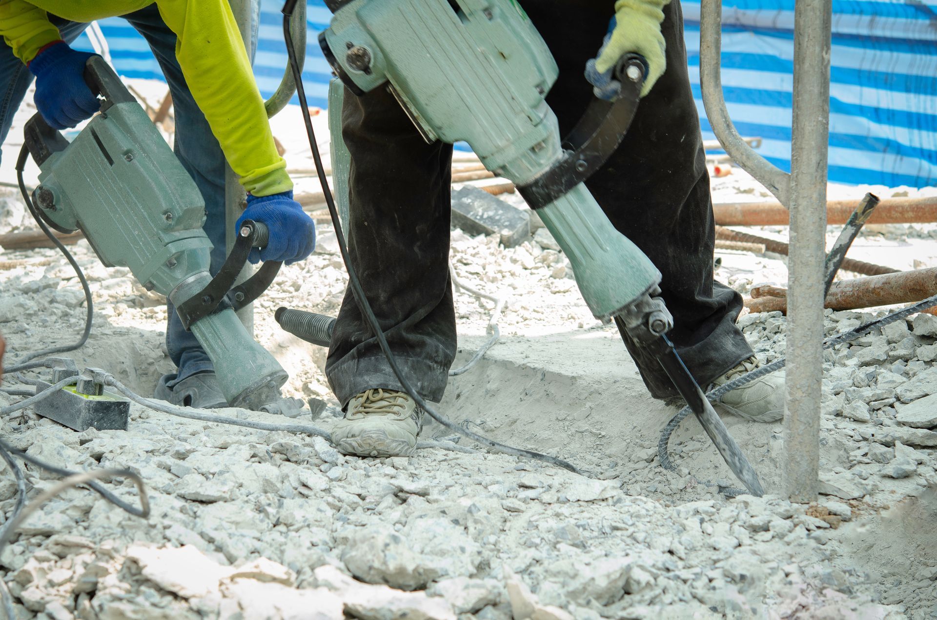 Two construction workers use heavy-duty jackhammers to break up concrete on a job site. Two construction workers use heavy-duty jackhammers to break up concrete on a job site.