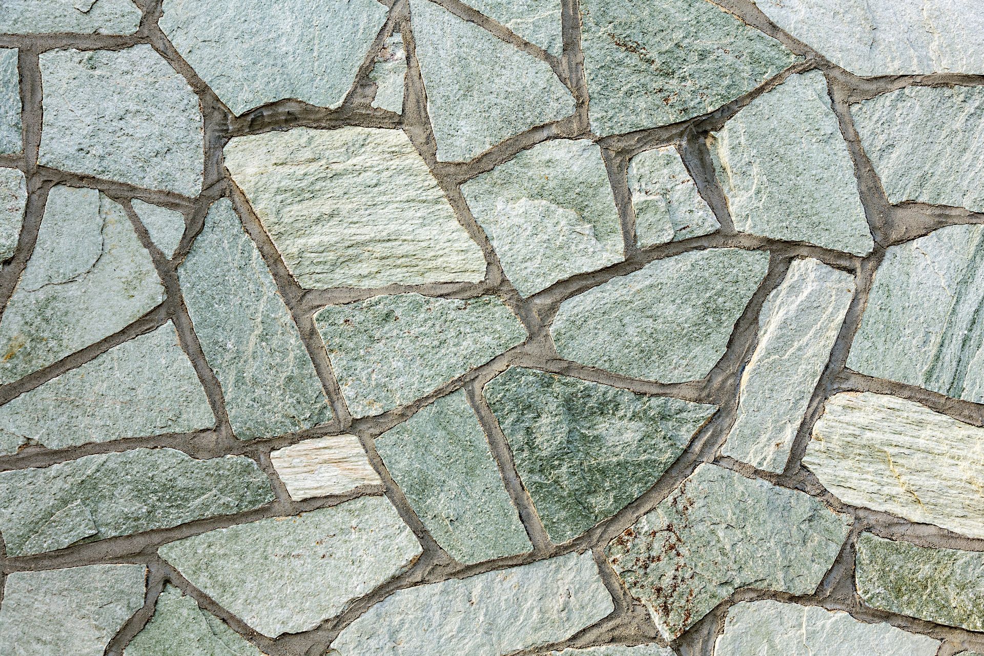 A surface covered in irregularly shaped, light green and grey natural stone tiles held together by dark grey mortar.