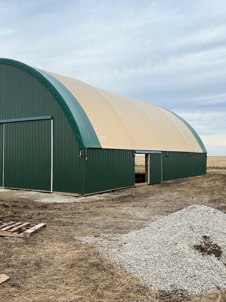 Green and beige arched metal storage building with open sliding doors.