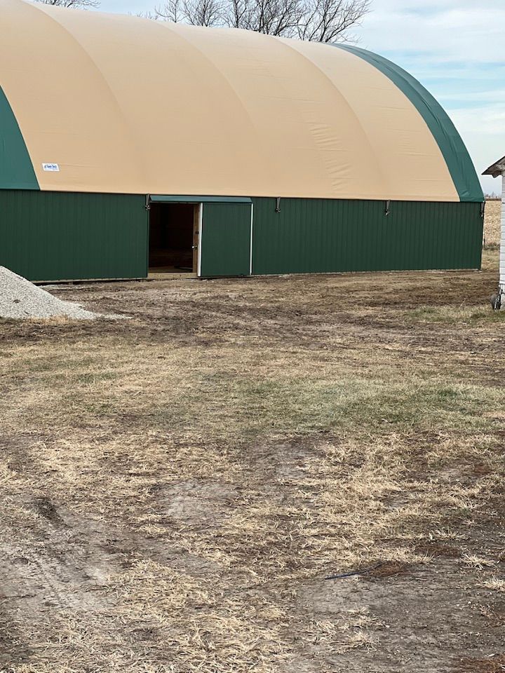 Green and tan arched building with open door, on a grassy plot.