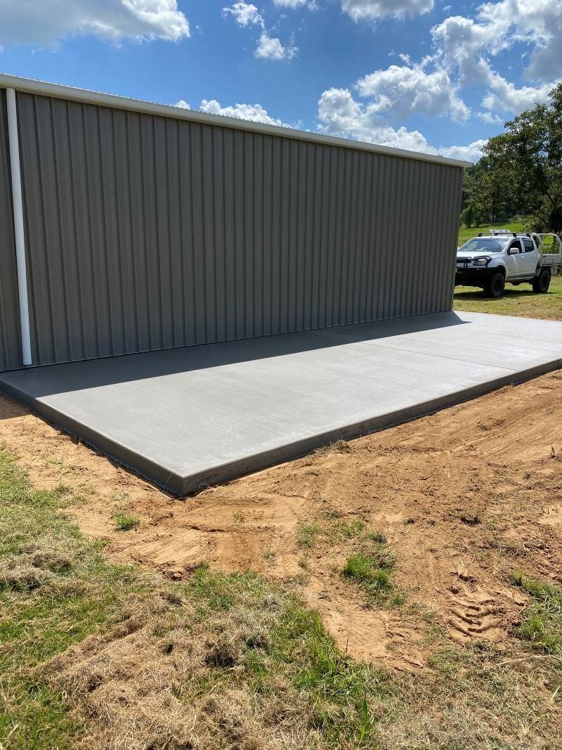 A Concrete Slab is Sitting in Front of a Metal Building — Peter Bishop Concreting In Gympie, QLD
