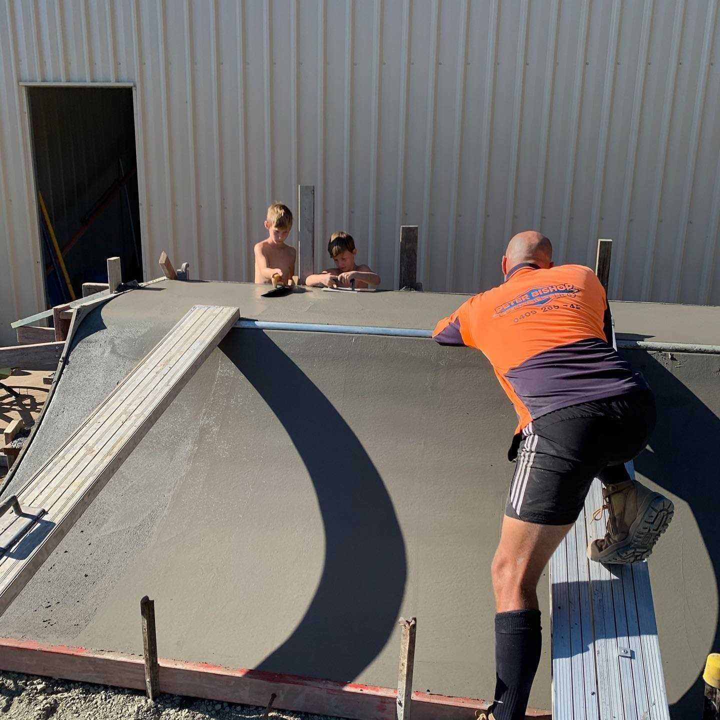 A Man in an Orange Shirt is Working on a Concrete Surface — Peter Bishop Concreting In Mary Valley, QLD