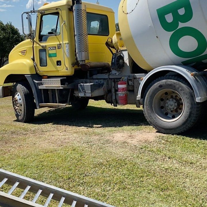 A Yellow Concrete Mixer Truck is Parked in a Grassy Field — Peter Bishop Concreting In Widgee, QLD