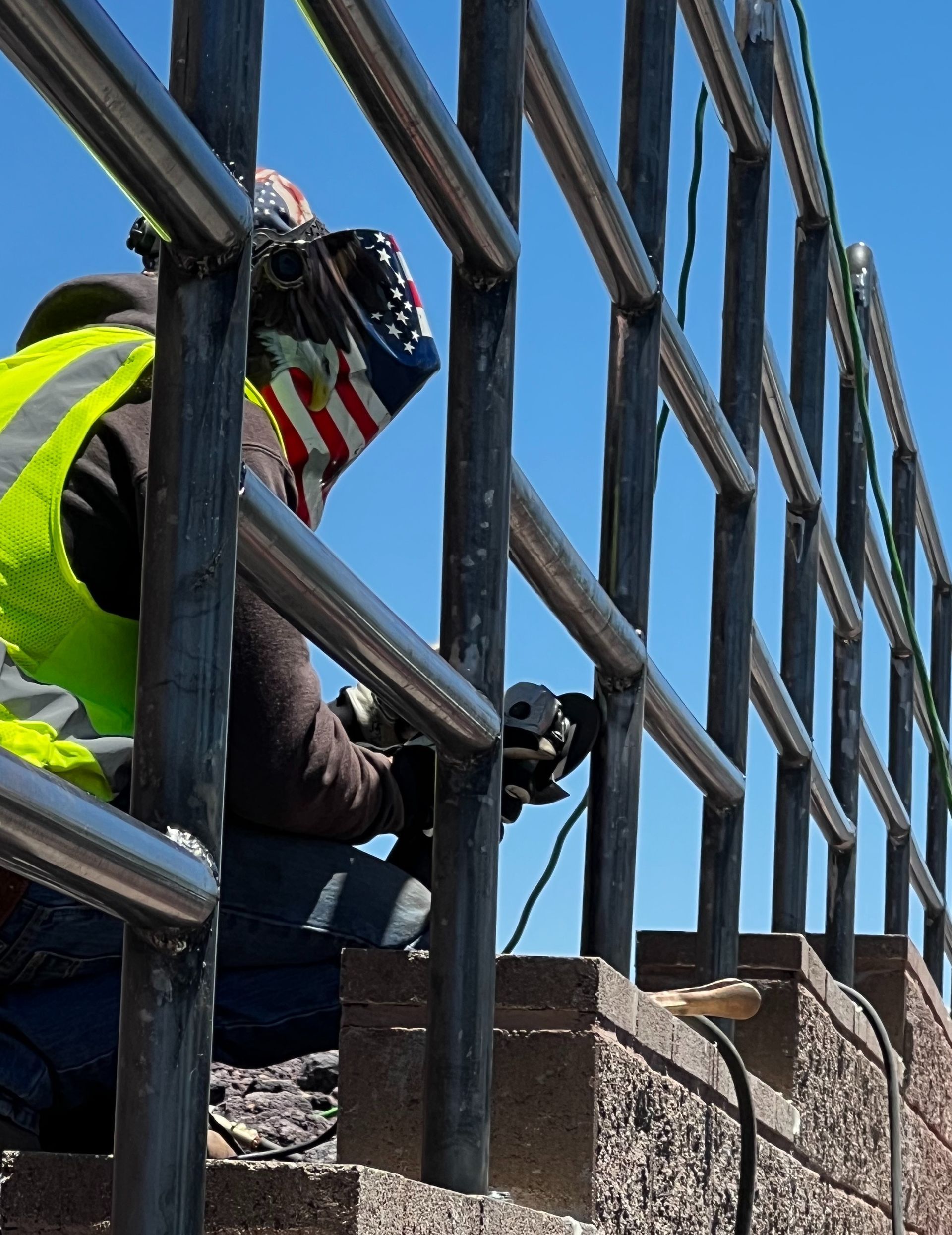 A man is welding a piece of metal with an american flag in the background.