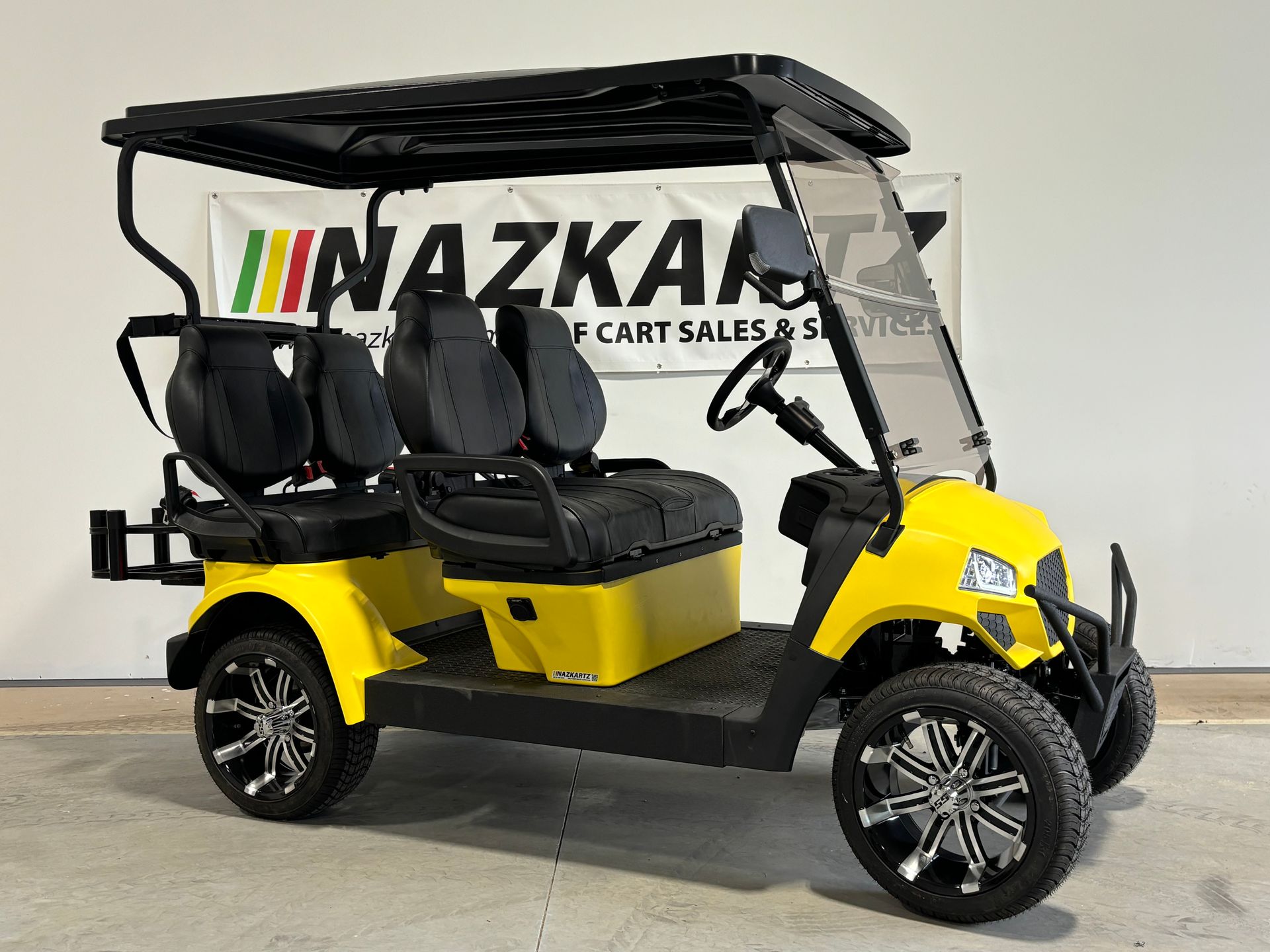 Yellow golf cart with black seats and roof, parked indoors.