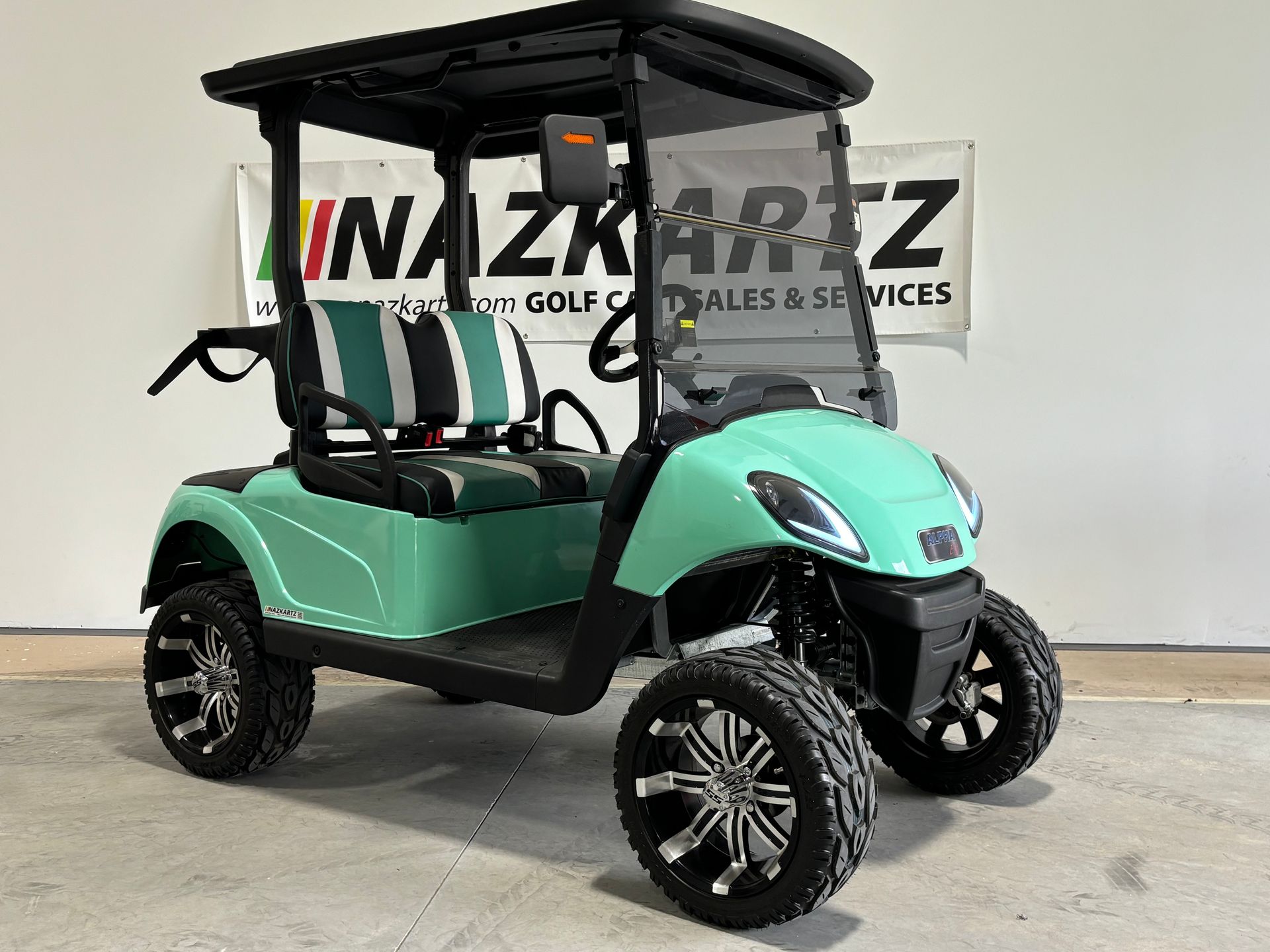 Aqua golf cart with black roof and wheels, parked inside, "INAZKARTZ" sign in background.