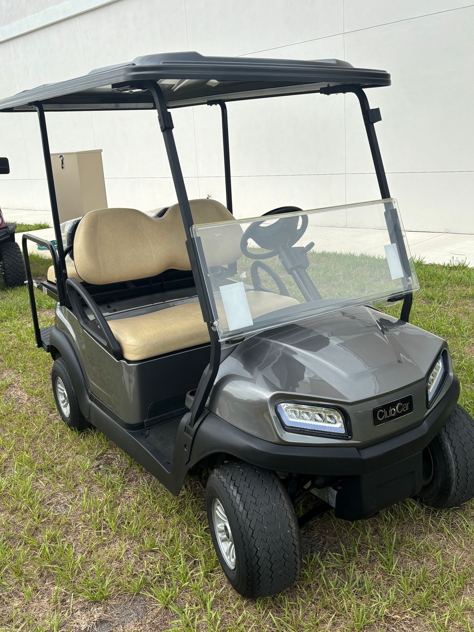 Gray golf cart with tan seats and windshield parked on grass.