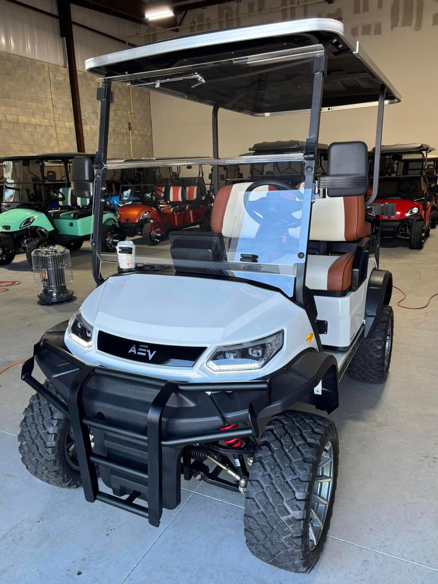 White and black golf cart with off-road tires, a black front bumper, and a roof, parked indoors.