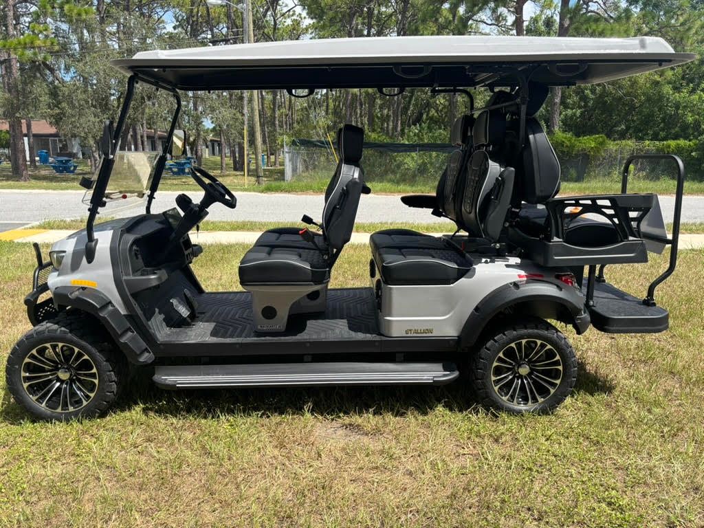 Red golf cart with brown seats, black roof, and off-road tires, parked on grass.