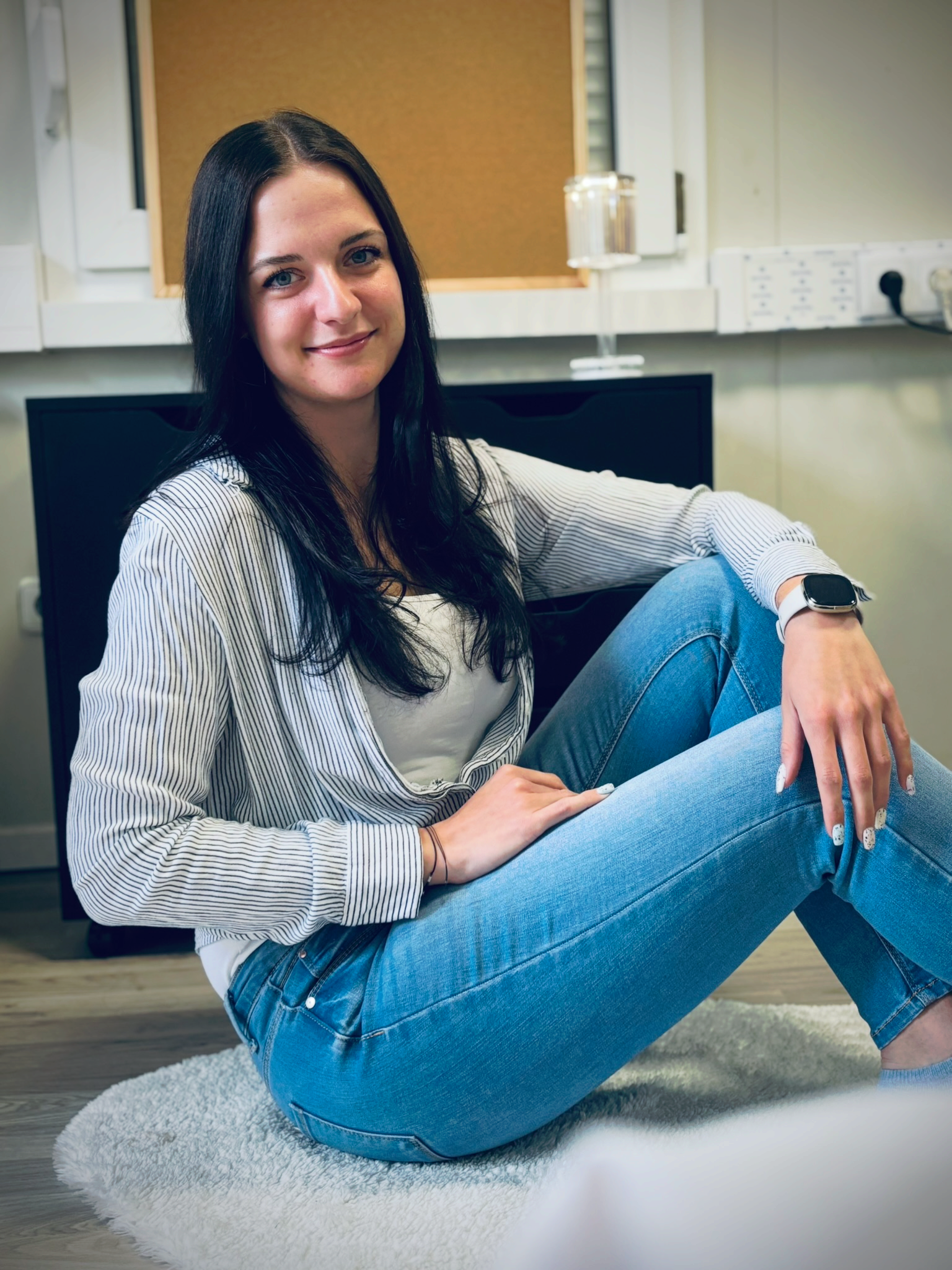 Eine Frau sitzt in Jeans und mit einer Uhr auf dem Boden.