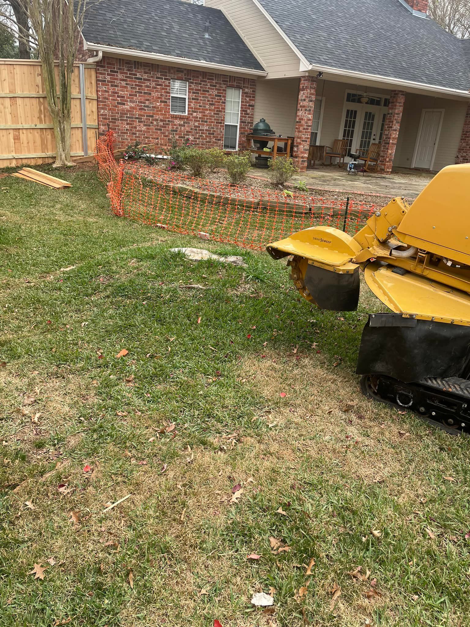 Yellow lawn mower on grass beside a brick house and flower bed