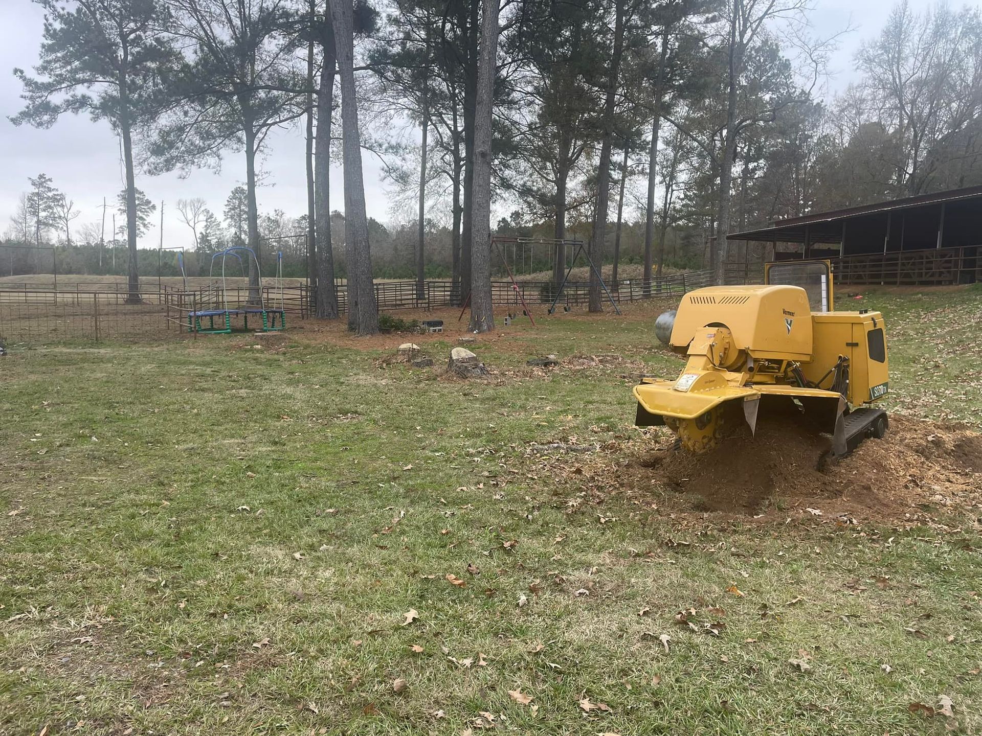 Yellow trailer in a grassy yard with tall trees and a barn in the background